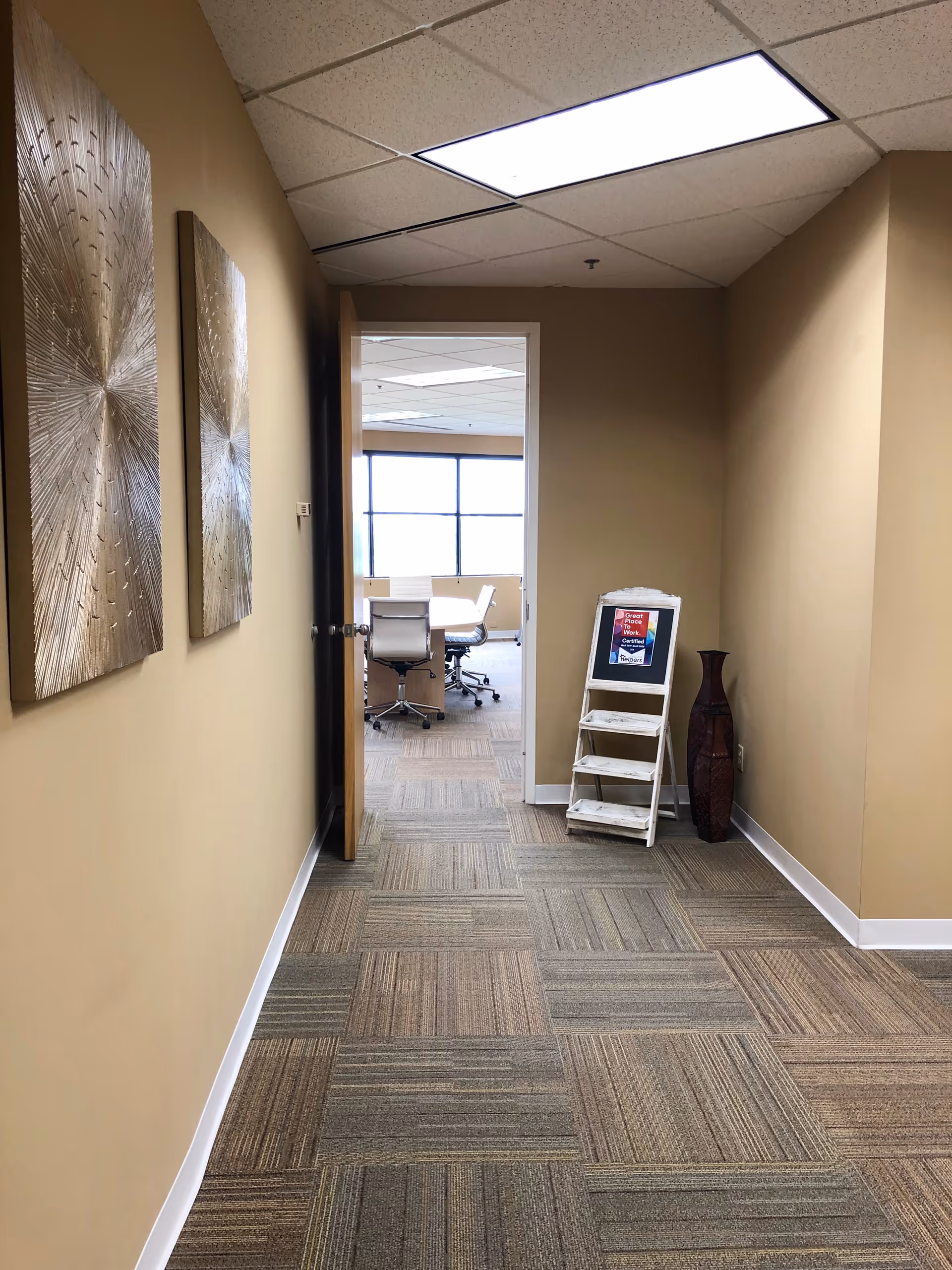 A beige hallway leads to a conference room with chairs and a windowed back area