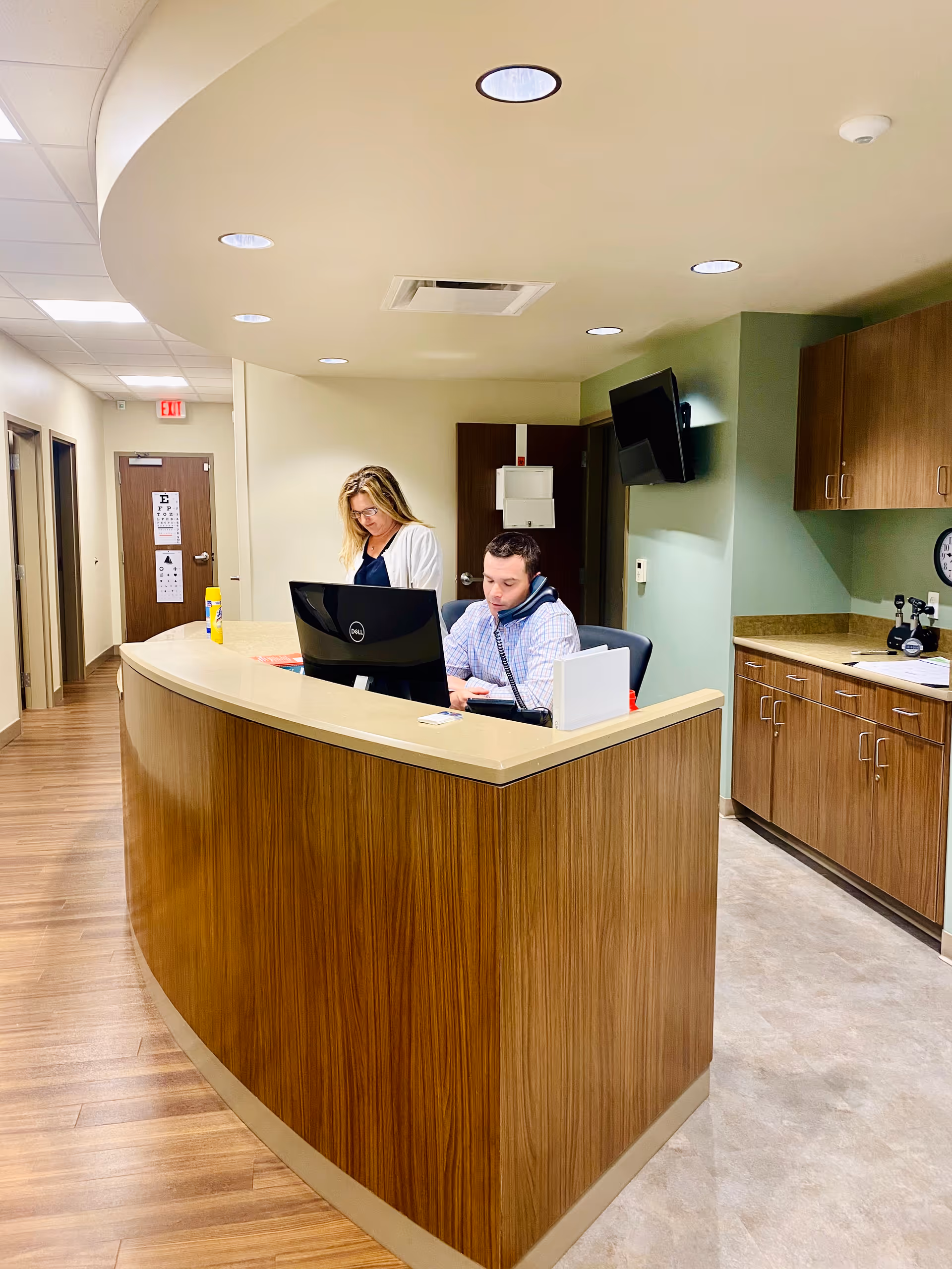 A curved wooden reception desk with two staff members in a modern facility lobby.