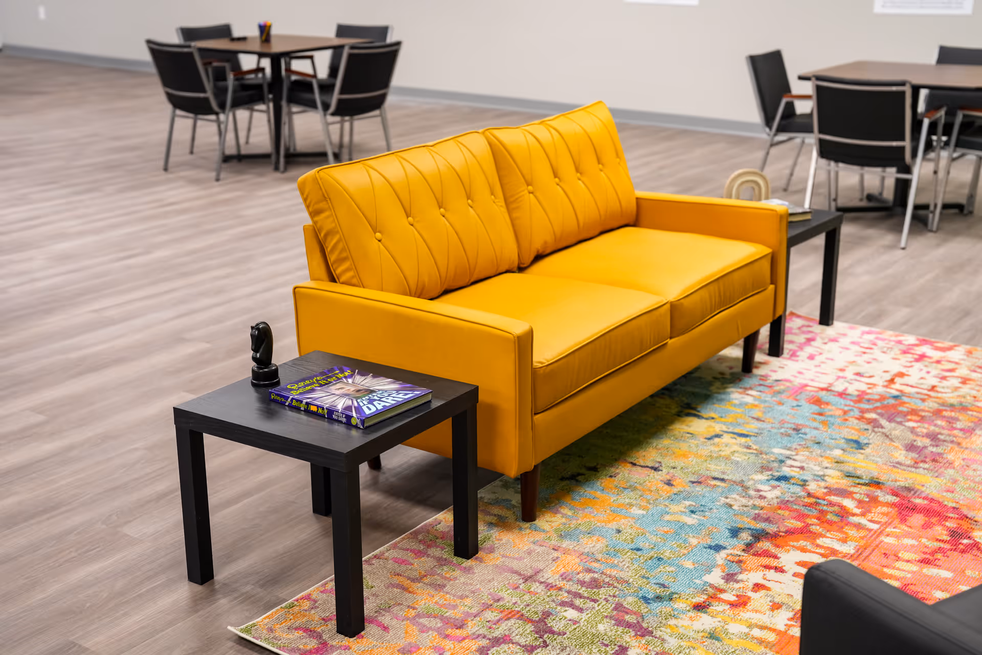 Bright yellow sofa sits in a lounge area with a colorful rug and black tables.
