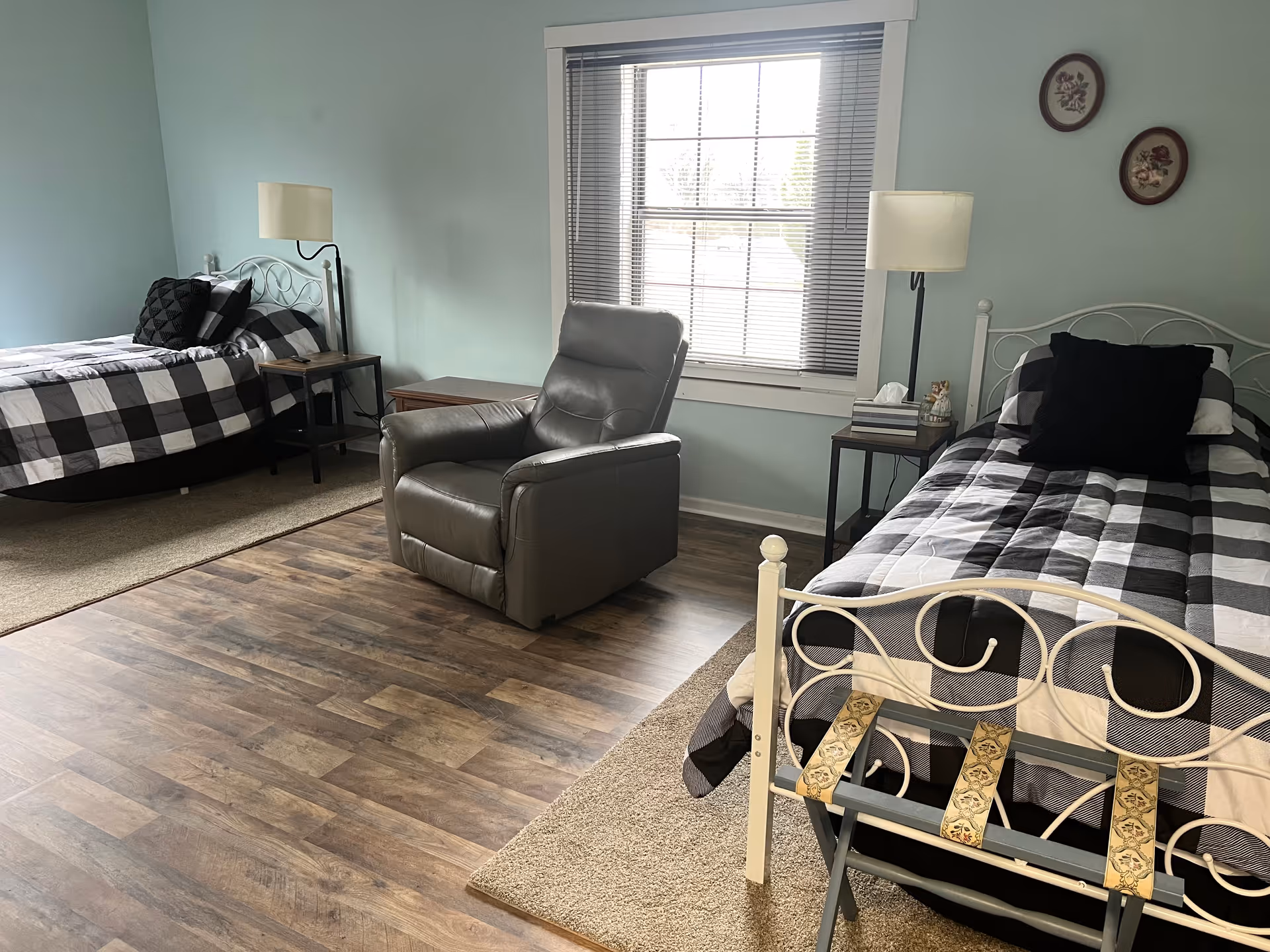 A shared bedroom with two metal-frame beds, a recliner, and side tables.