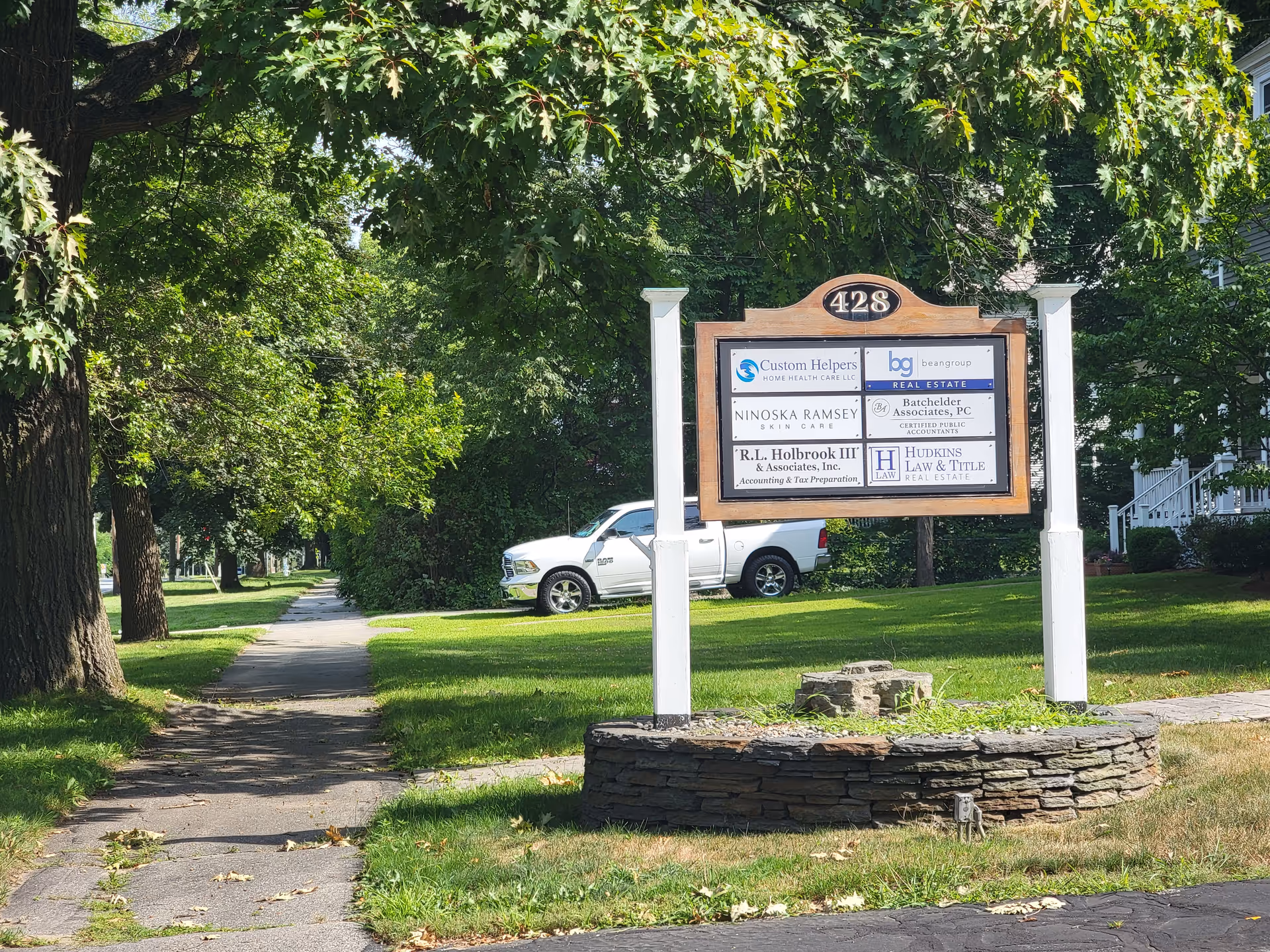 Outdoor street scene with a large signboard on a grassy lawn and trees.