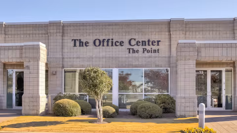 Front exterior of a brick office building with large windows and trimmed shrubs.