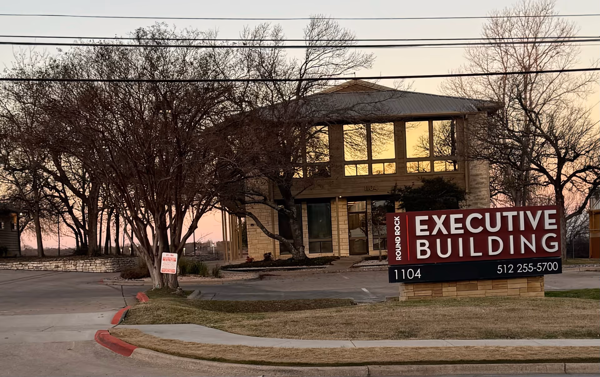 Exterior view of a two-story stone building with a large red Executive Building sign in front.