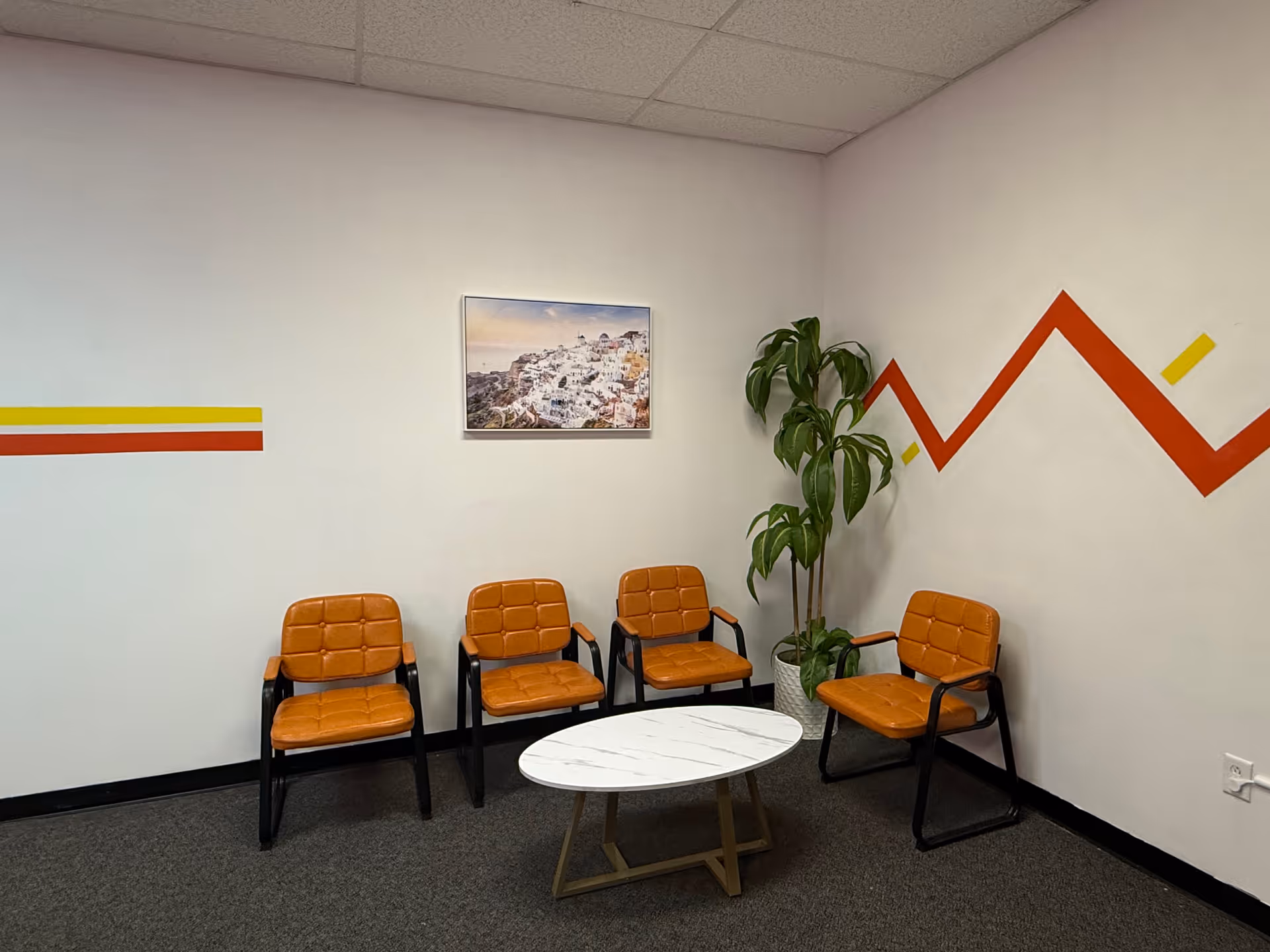 A small waiting area with orange cushioned chairs around a white round marble coffee table.