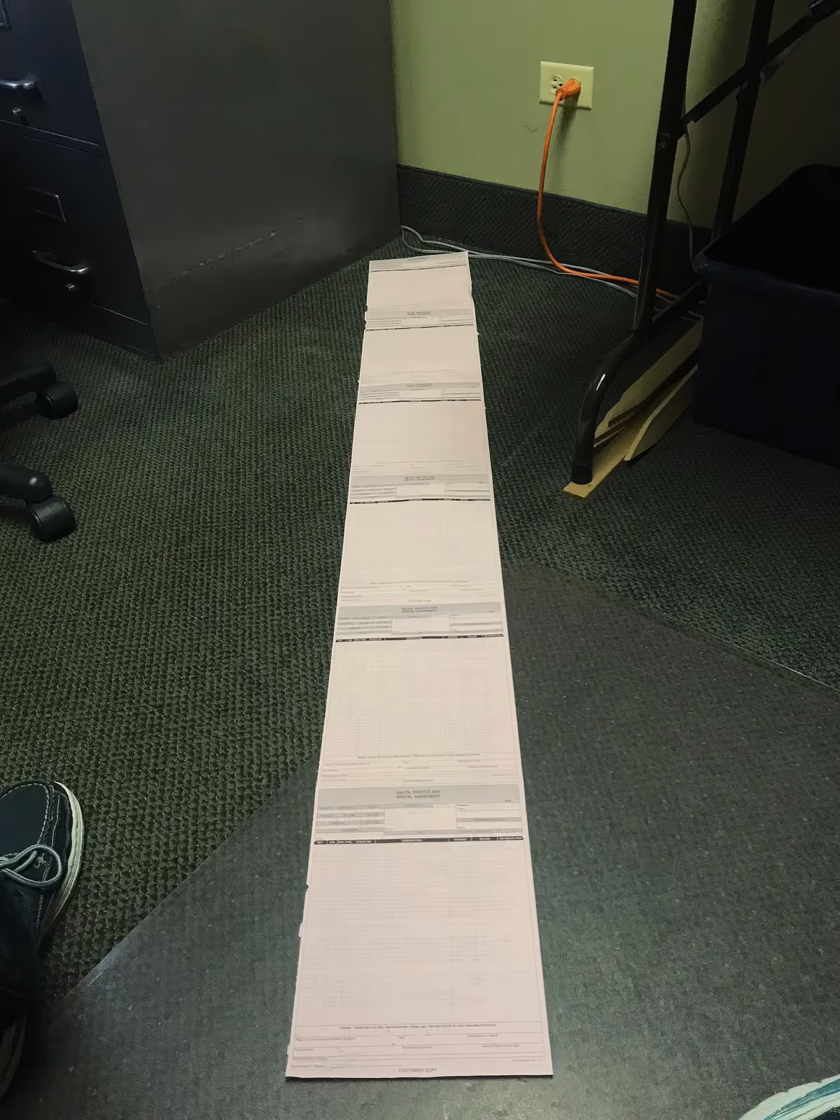 A long row of printed forms extends along a green-carpeted office floor.