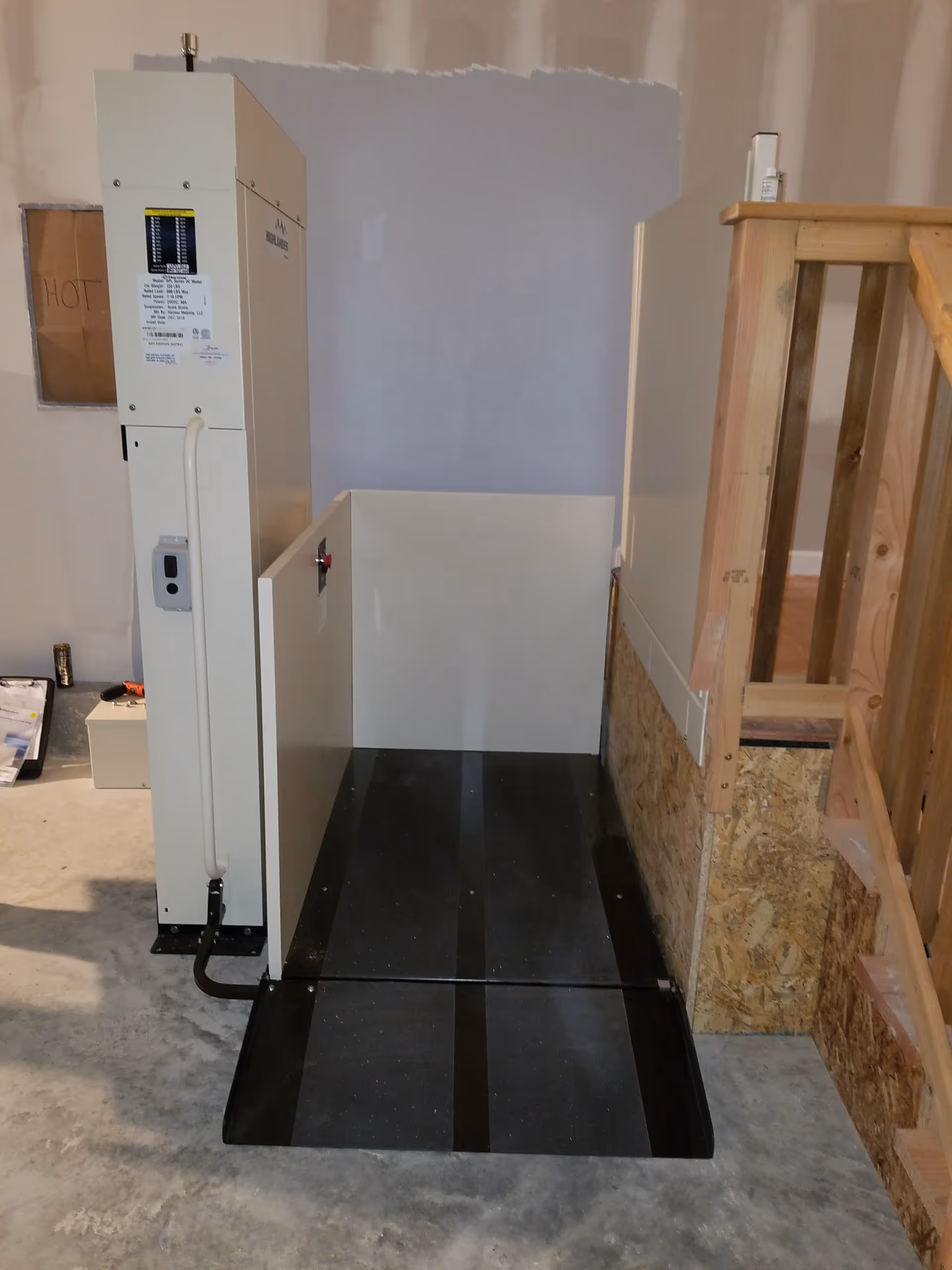 Unfinished interior showing a vertical lift platform beside a wooden staircase.