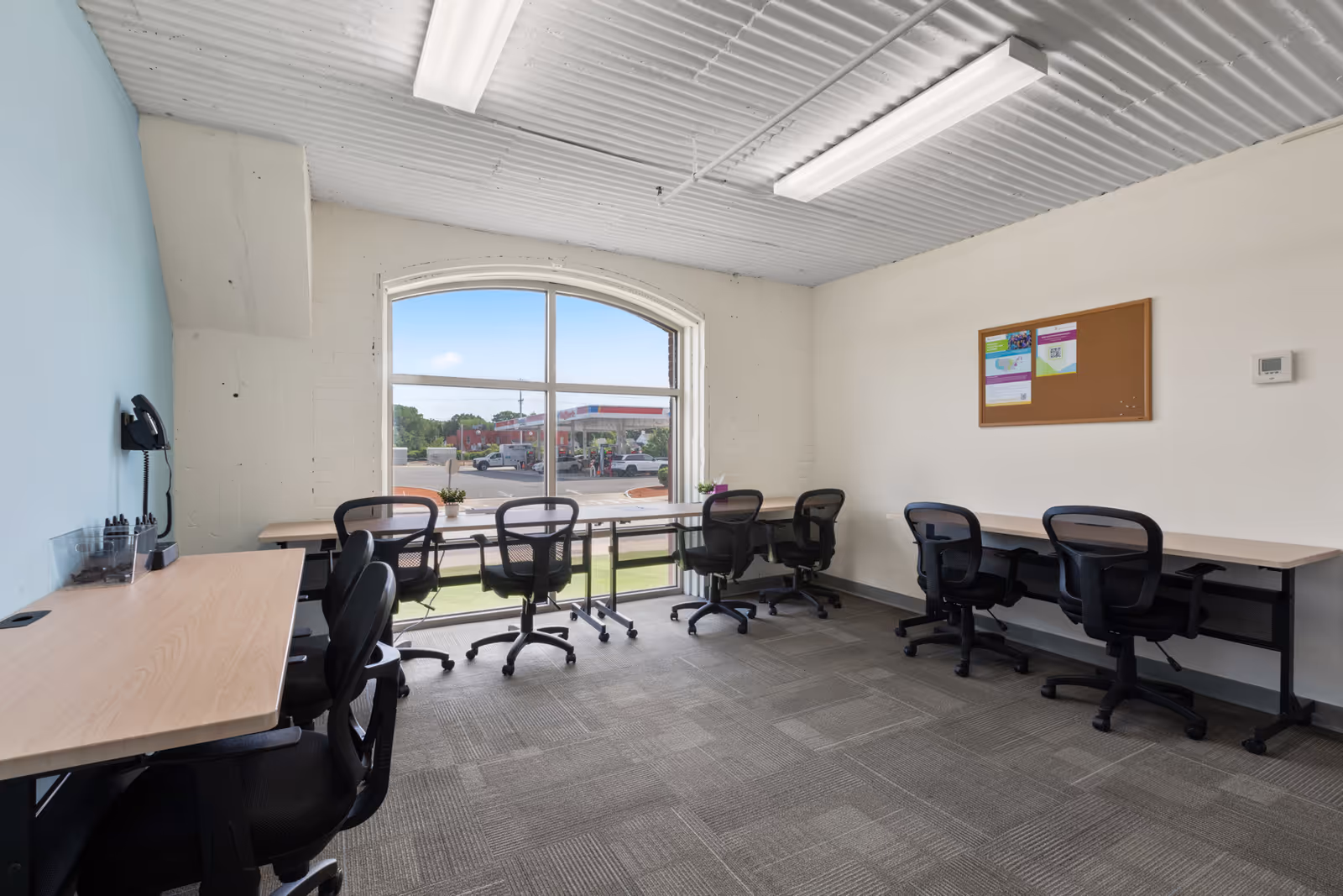 Bright interior with long desks and multiple chairs along a large windowed wall.
