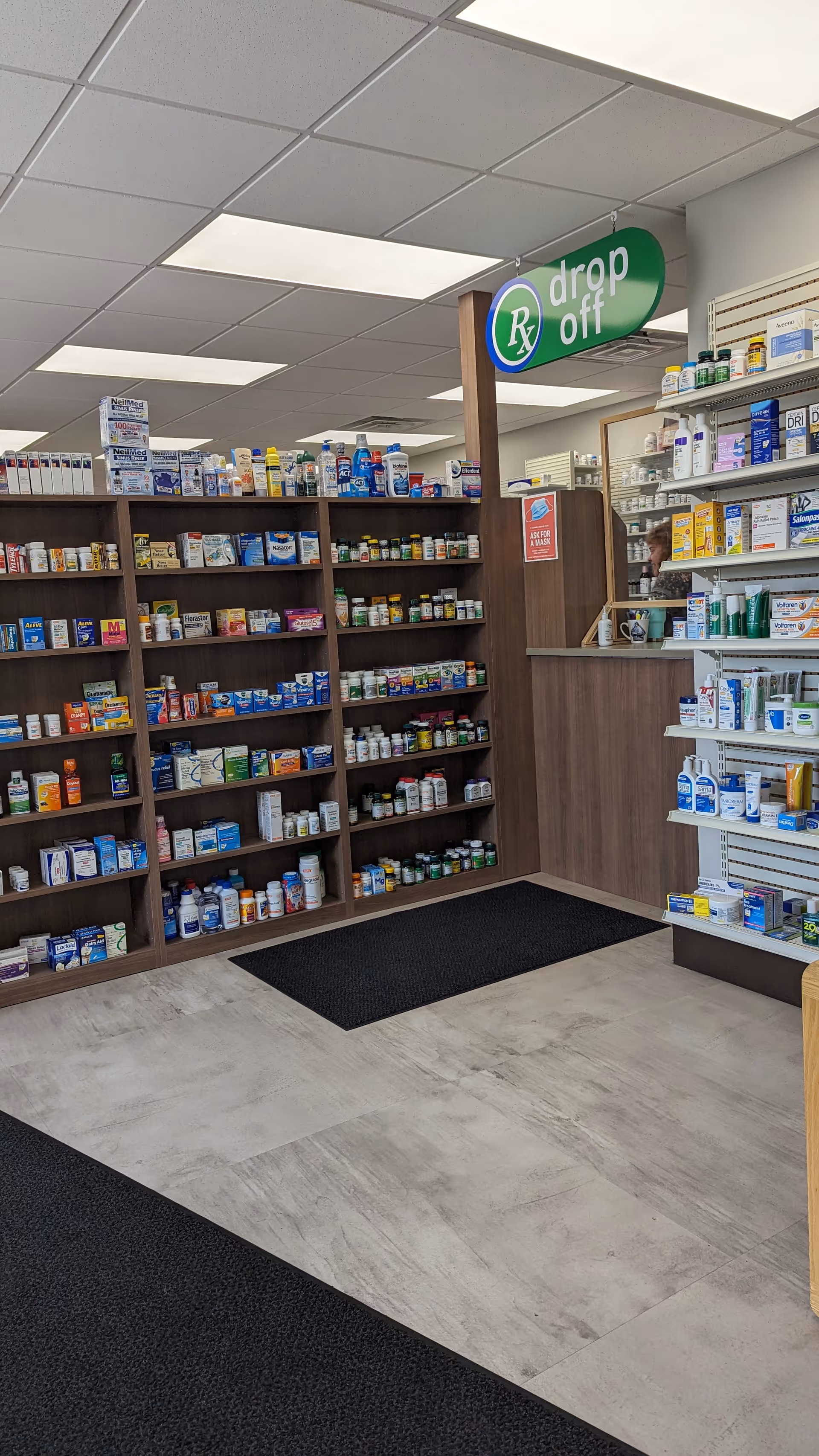 Interior view of a medical center pharmacy with wall shelves of medications and a drop-off sign.