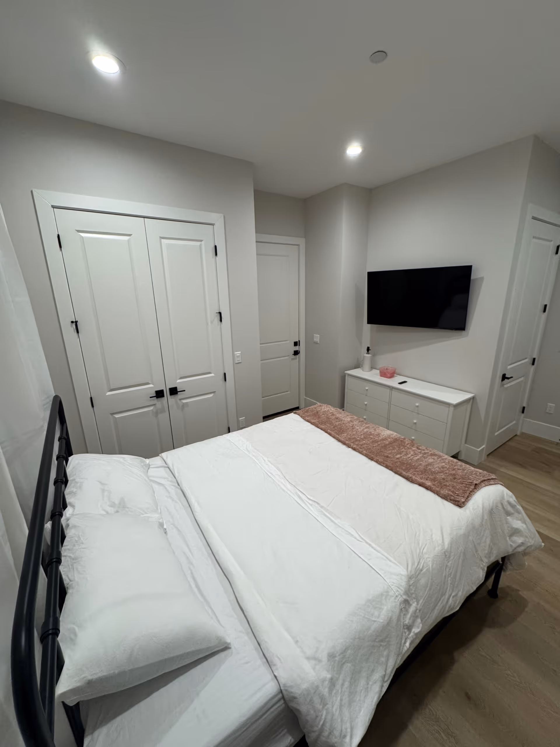 A clean, modern bedroom with a bed, dresser, wall-mounted TV, and neutral decor.