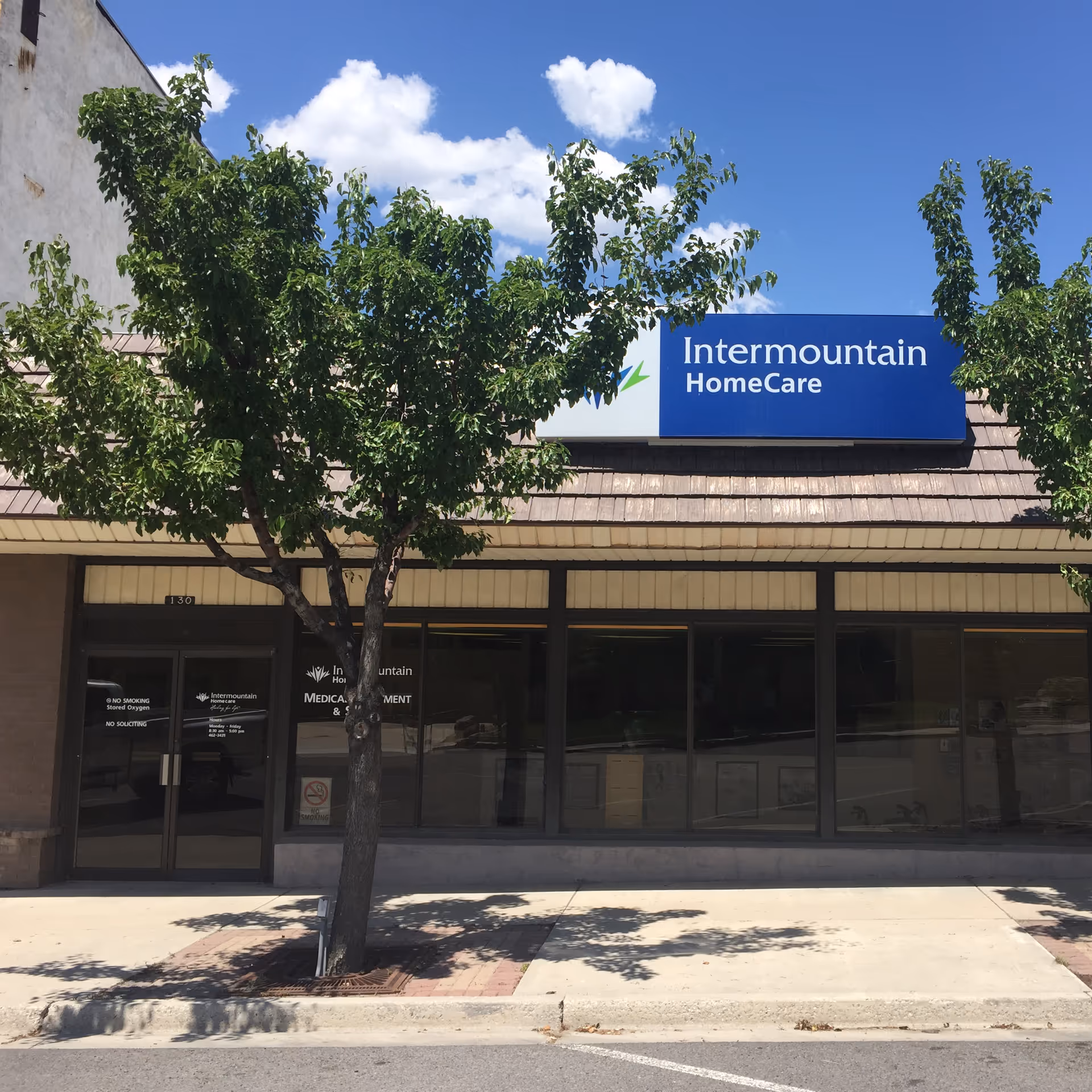 Facade of Intermountain HomeCare storefront with trees and a blue sign.