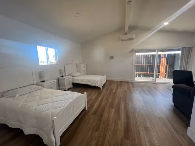 Two white twin beds with matching nightstands and dresser fill a bedroom with a patio door.