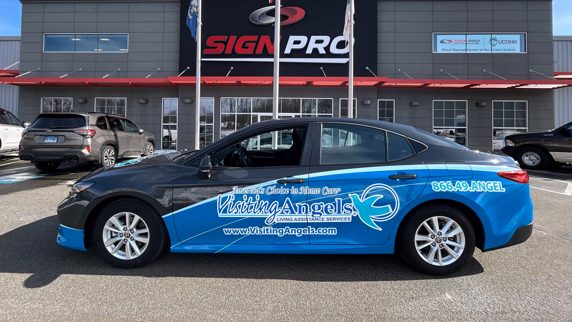 Blue Visiting Angels promotional car parked outside a building with signage