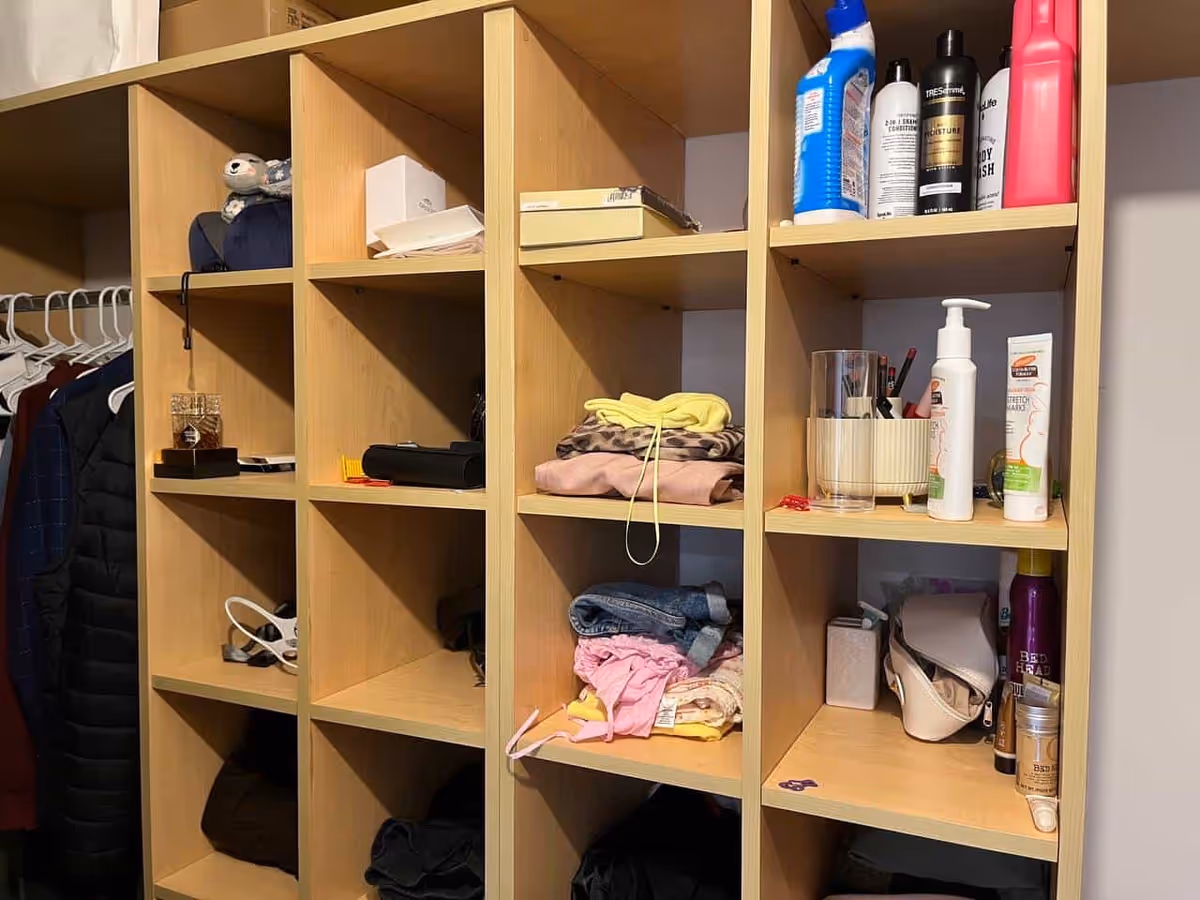 Open wooden cubby storage with clothes, toiletries, and miscellaneous items in a facility closet.