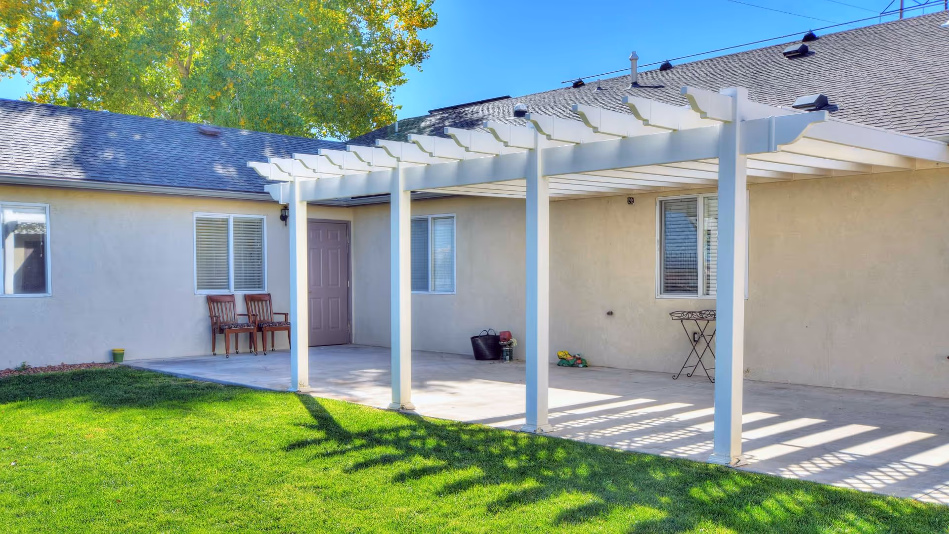 Exterior view of a single-story senior living building with a white pergola and grassy yard