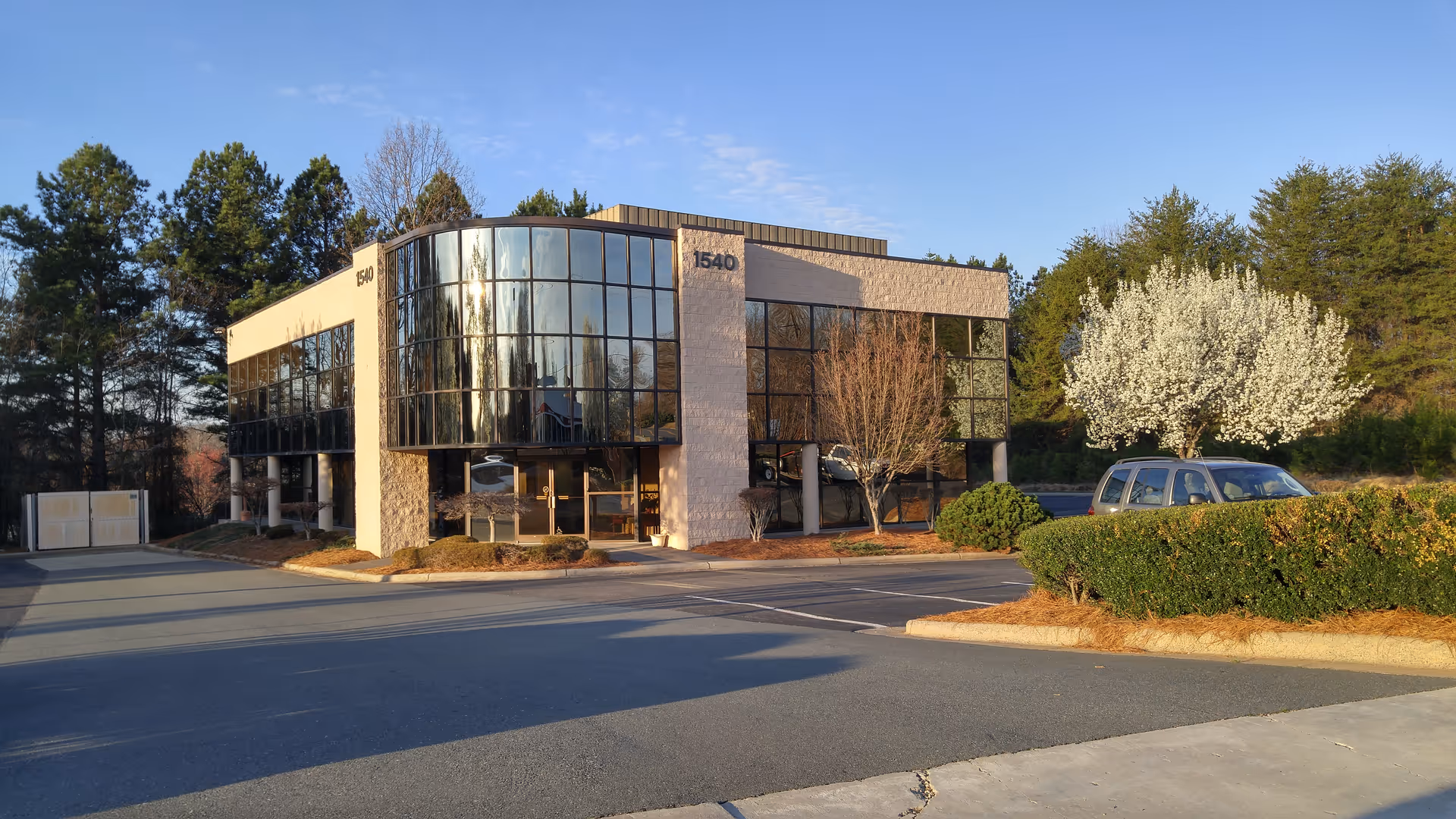 Exterior view of a modern glass-front senior home care building with parking and landscaping