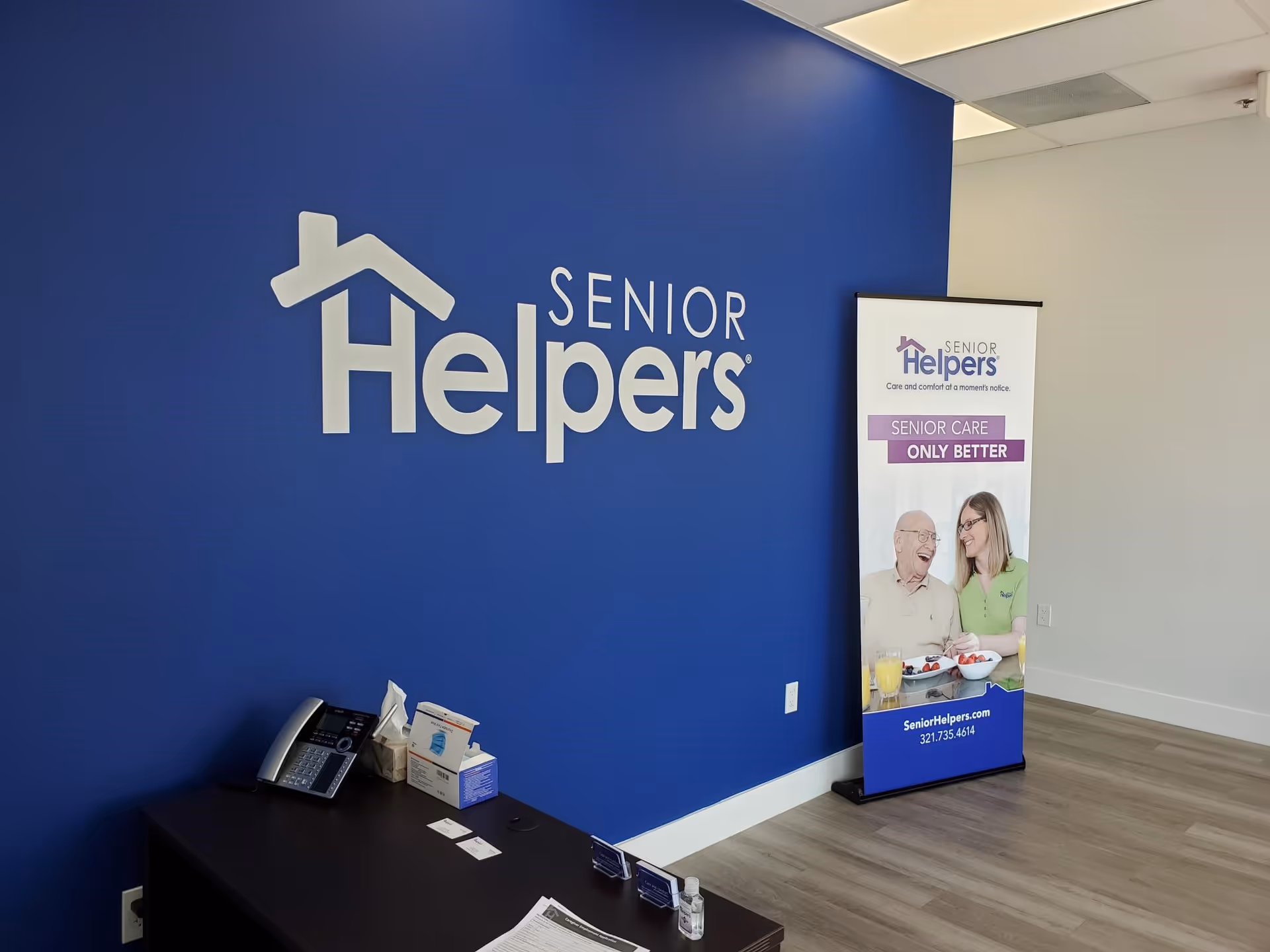 Blue wall with Senior Helpers logo beside a standing banner in a reception area.