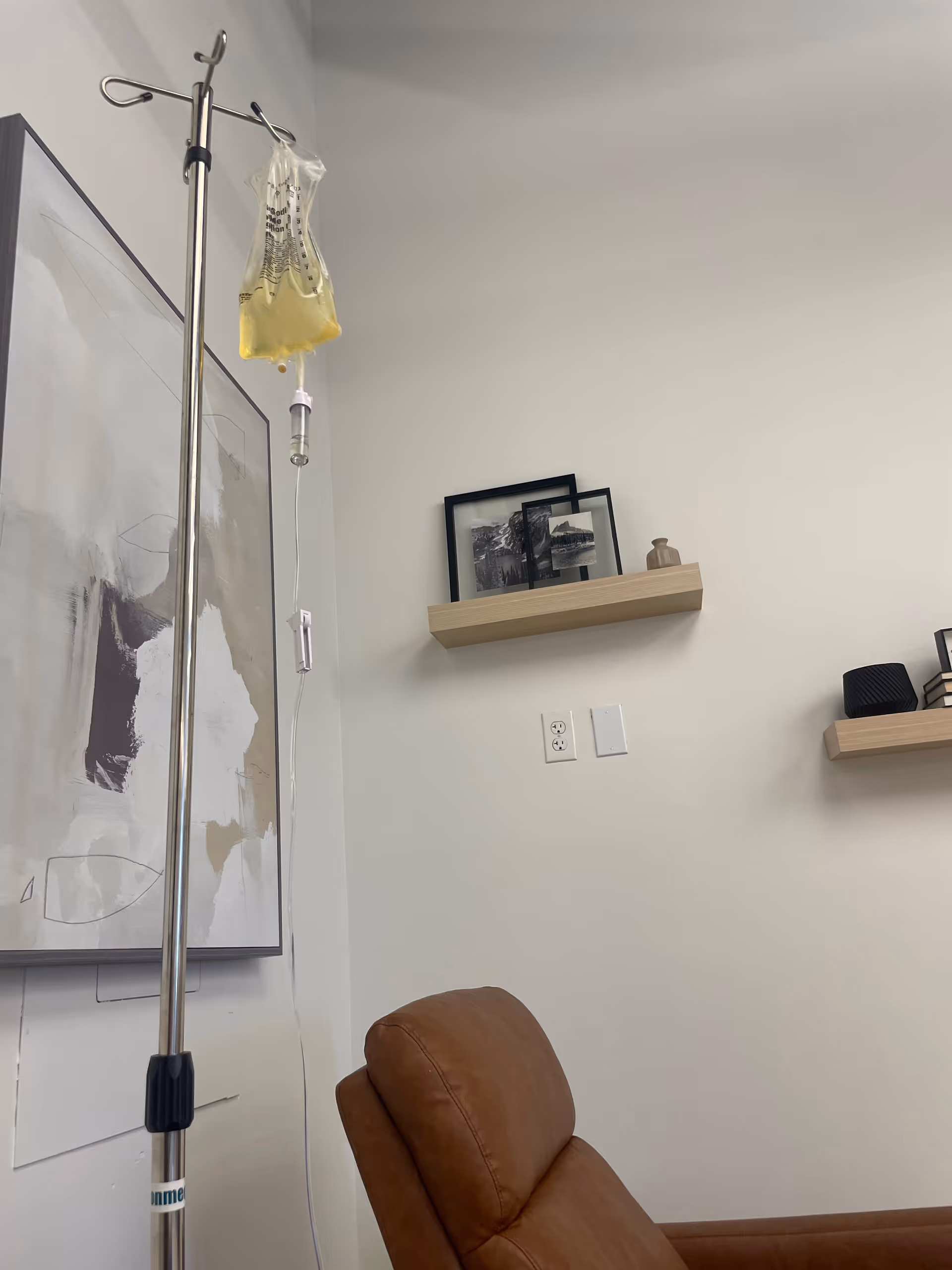 IV pole with hanging bag beside a brown recliner in a medical treatment room.