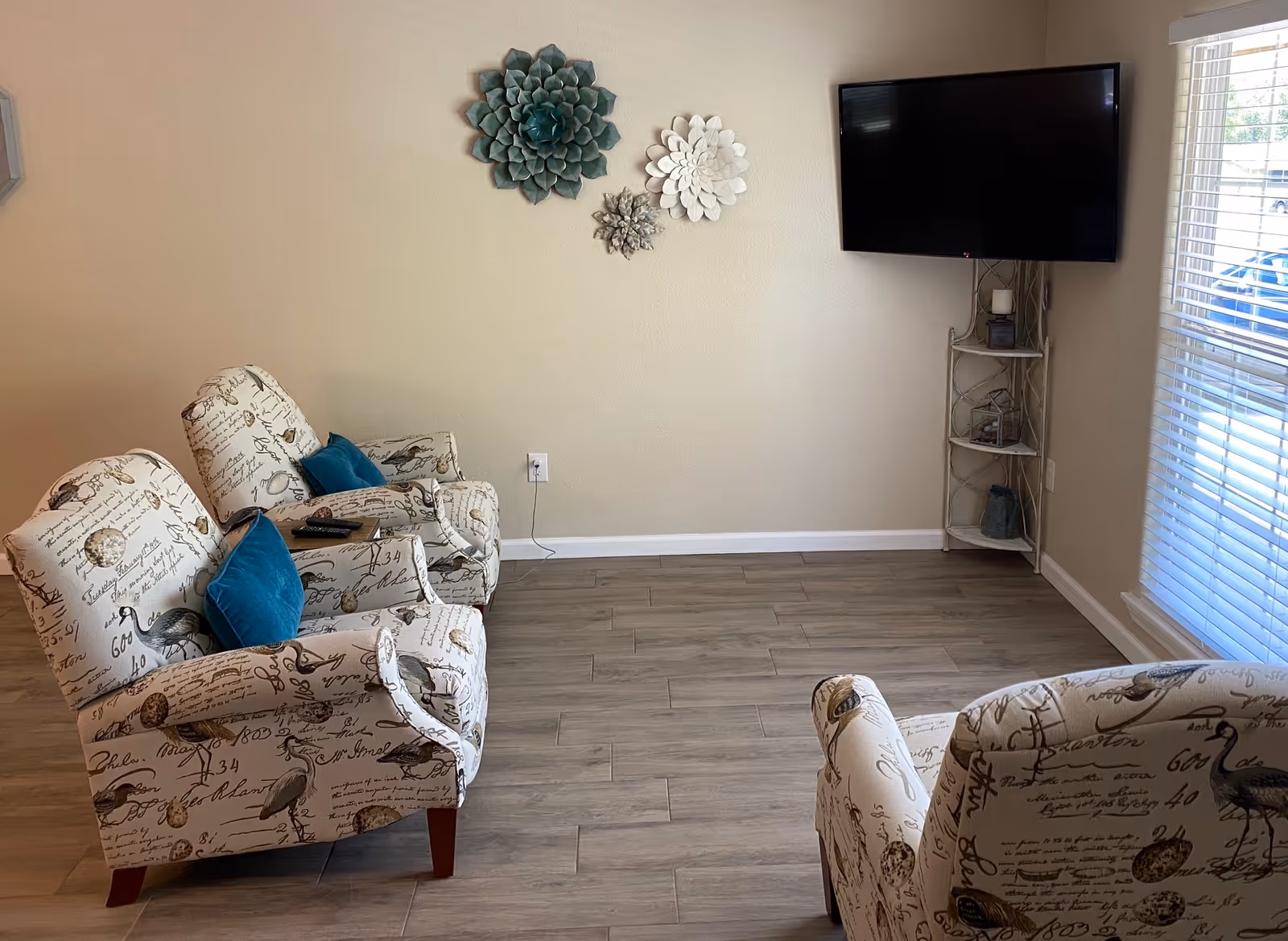 Cozy living room with patterned chairs, teal cushions, wall decor, and a wall-mounted TV.