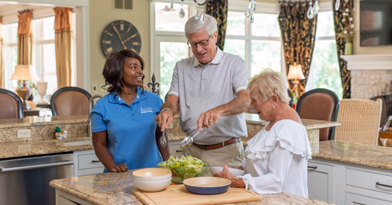 Staff member and two residents prepare salad together in a bright, modern kitchen.