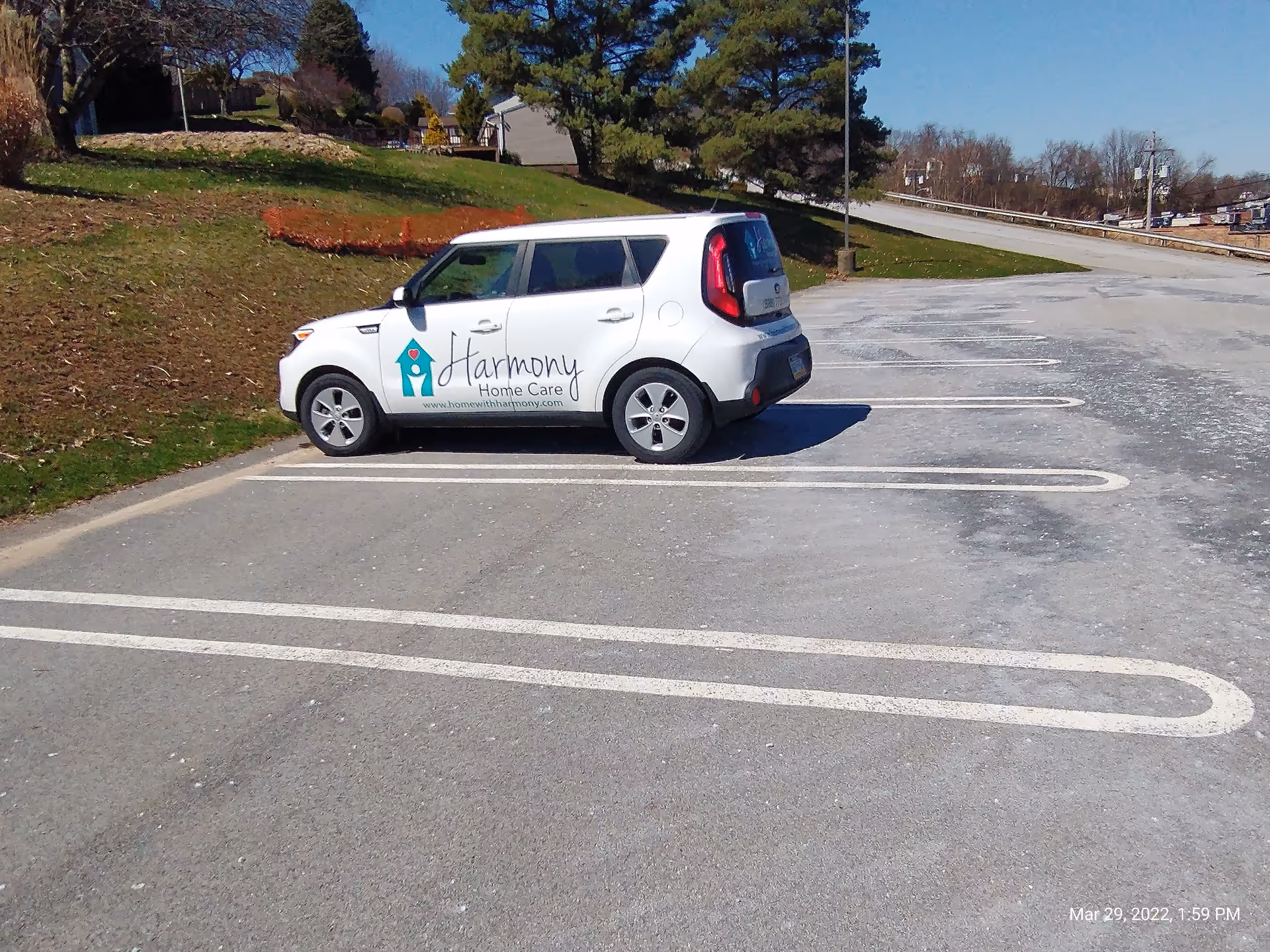 A white Harmony Home Care car parked diagonally in an empty outdoor parking lot.