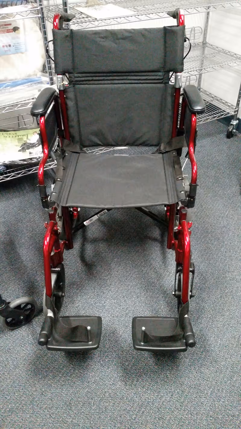 Wheelchair with red frame and black seat inside a facility near shelving