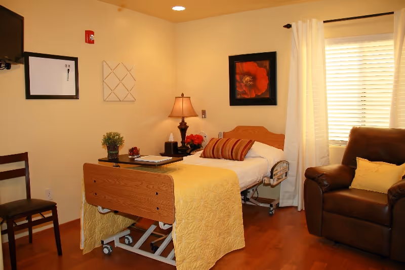 A hospital-style bedroom with a single bed, yellow quilt, lamp, and leather chair.