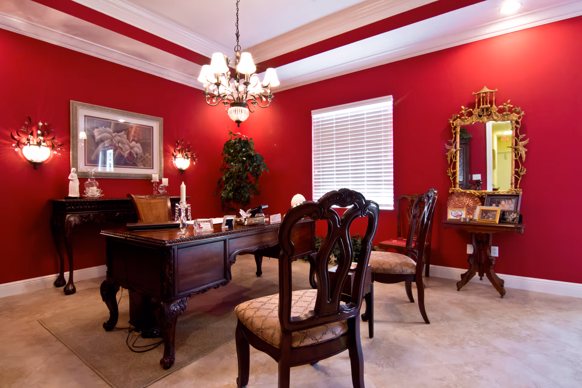 Elegant dining room with dark wood table, ornate chairs, red walls, chandelier.