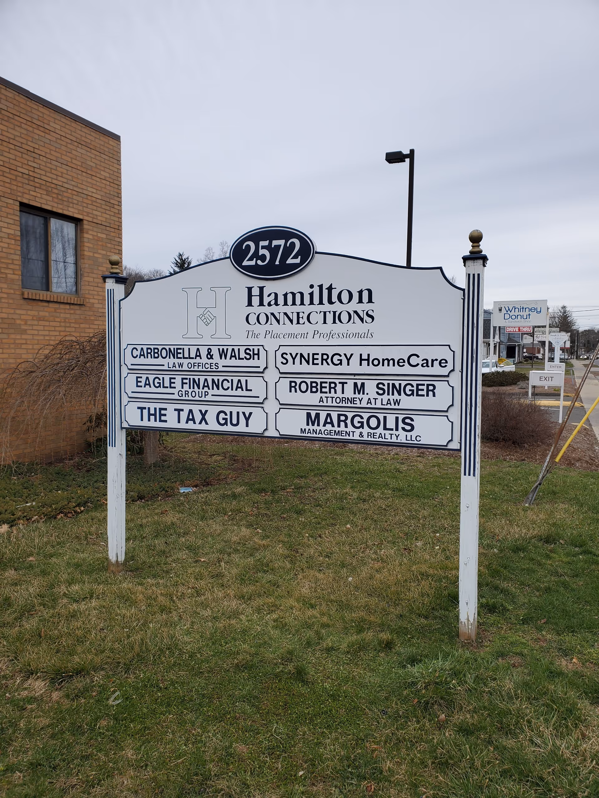 Outdoor sign displays Hamilton Connections and Synergy HomeCare near a brick building