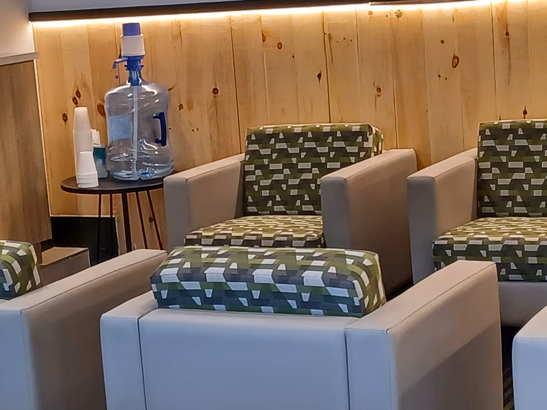 Lobby seating area with white armchairs, green patterned cushions, and a water jug on a table.