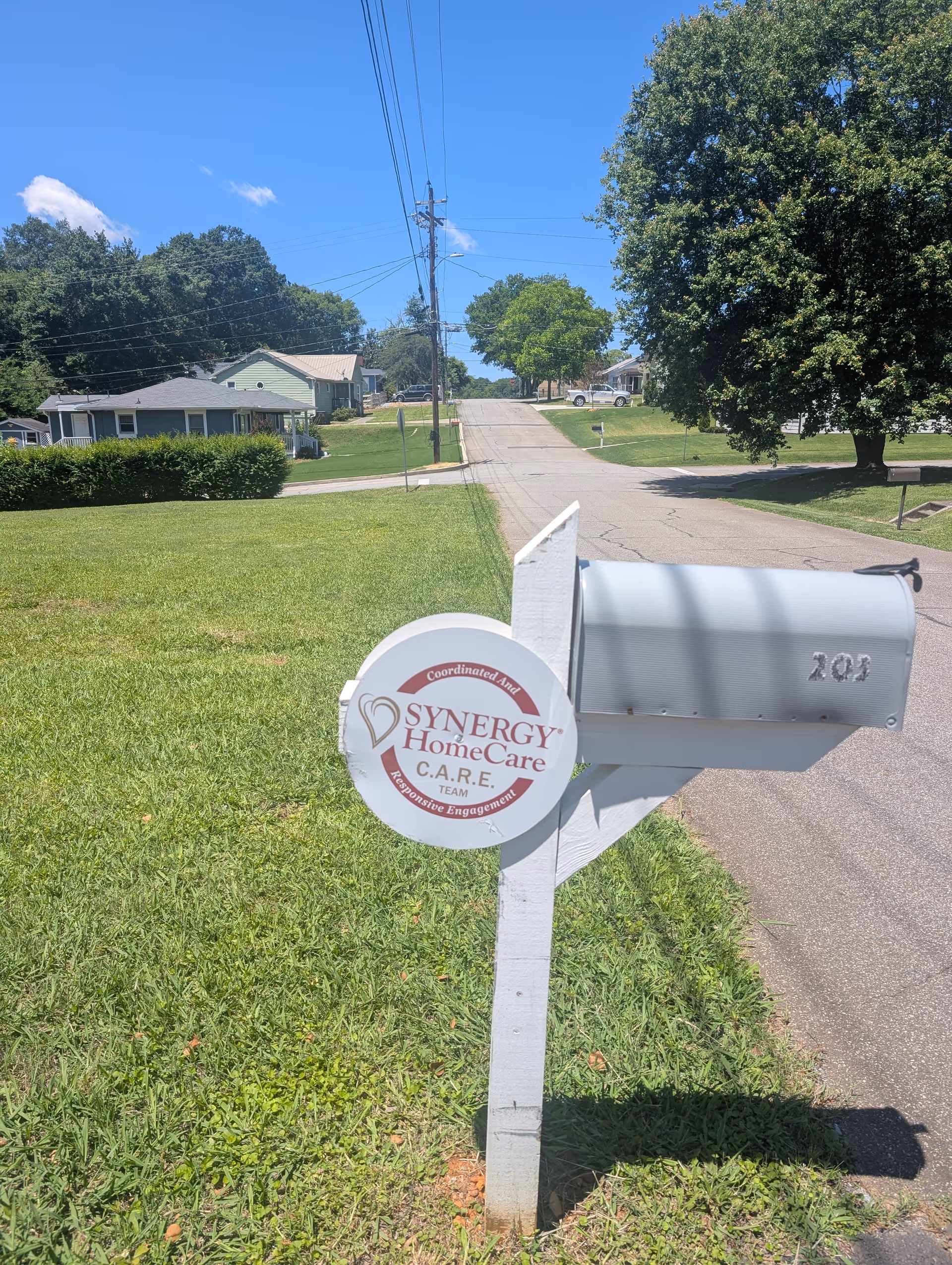 Residential street view with a Synergy HomeCare mailbox sign beside a curb.