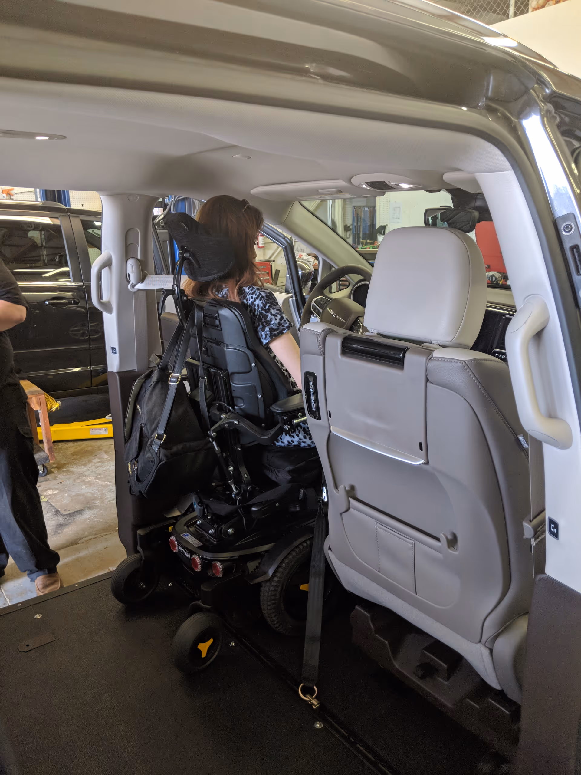 Inside a van, a person in a powered wheelchair sits near the driver's seat.
