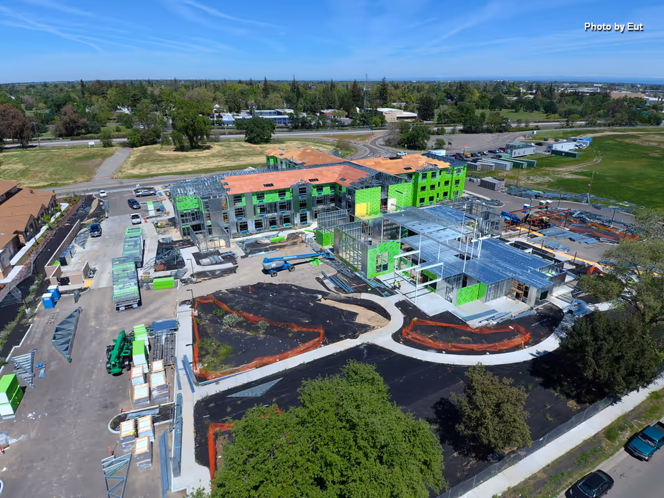 Aerial view of a senior living construction site with green-framed buildings and curved driveway.