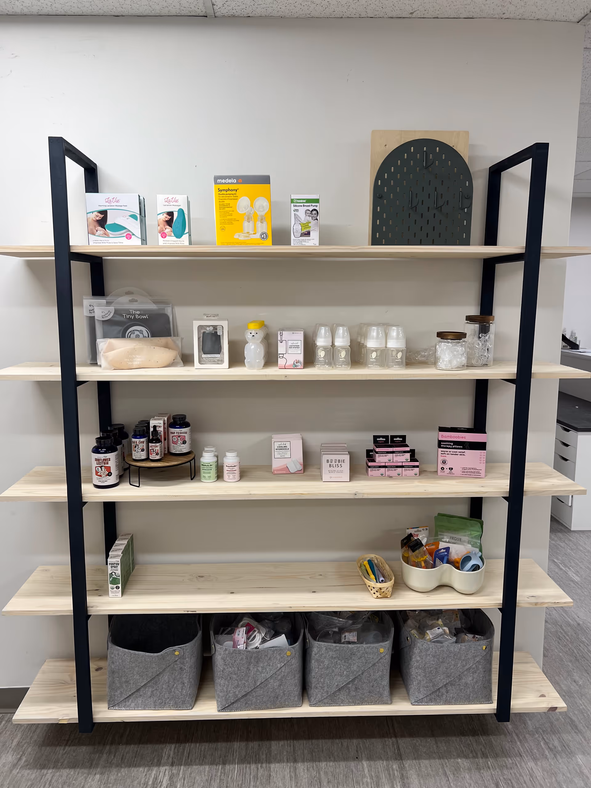 Open wooden shelves hold infant feeding products and assorted small medical supplies.