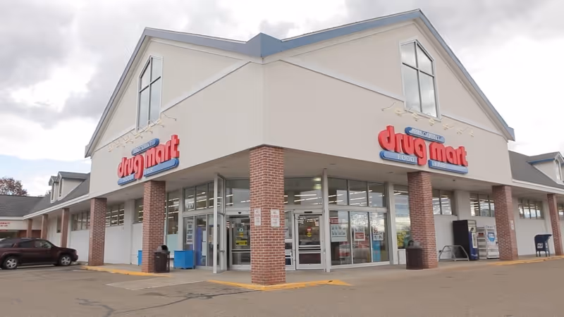 Exterior view of Discount Drug Mart storefront with brick columns and glass entrance.
