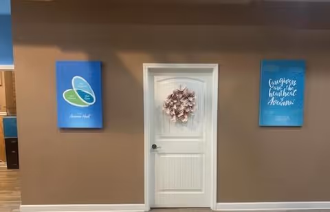 Brown interior wall with a white door decorated with a wreath, flanked by blue posters.
