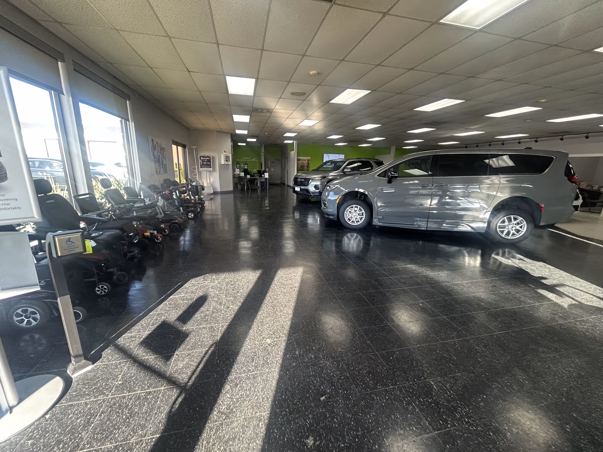 Indoor showroom with scooters and wheelchairs along the left and parked minivans on the right