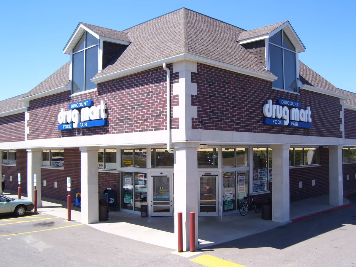 Brick Discount Drug Mart storefront with glass entry doors and parking in front.
