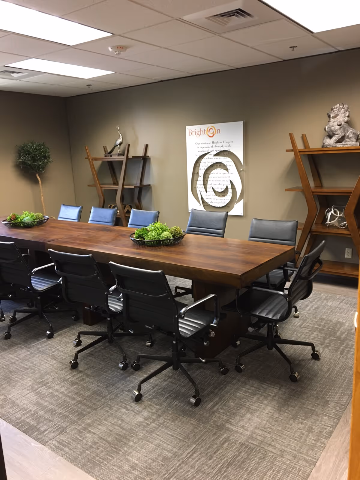 A large conference room with a wooden table, black chairs, shelves, and a Brighton poster.