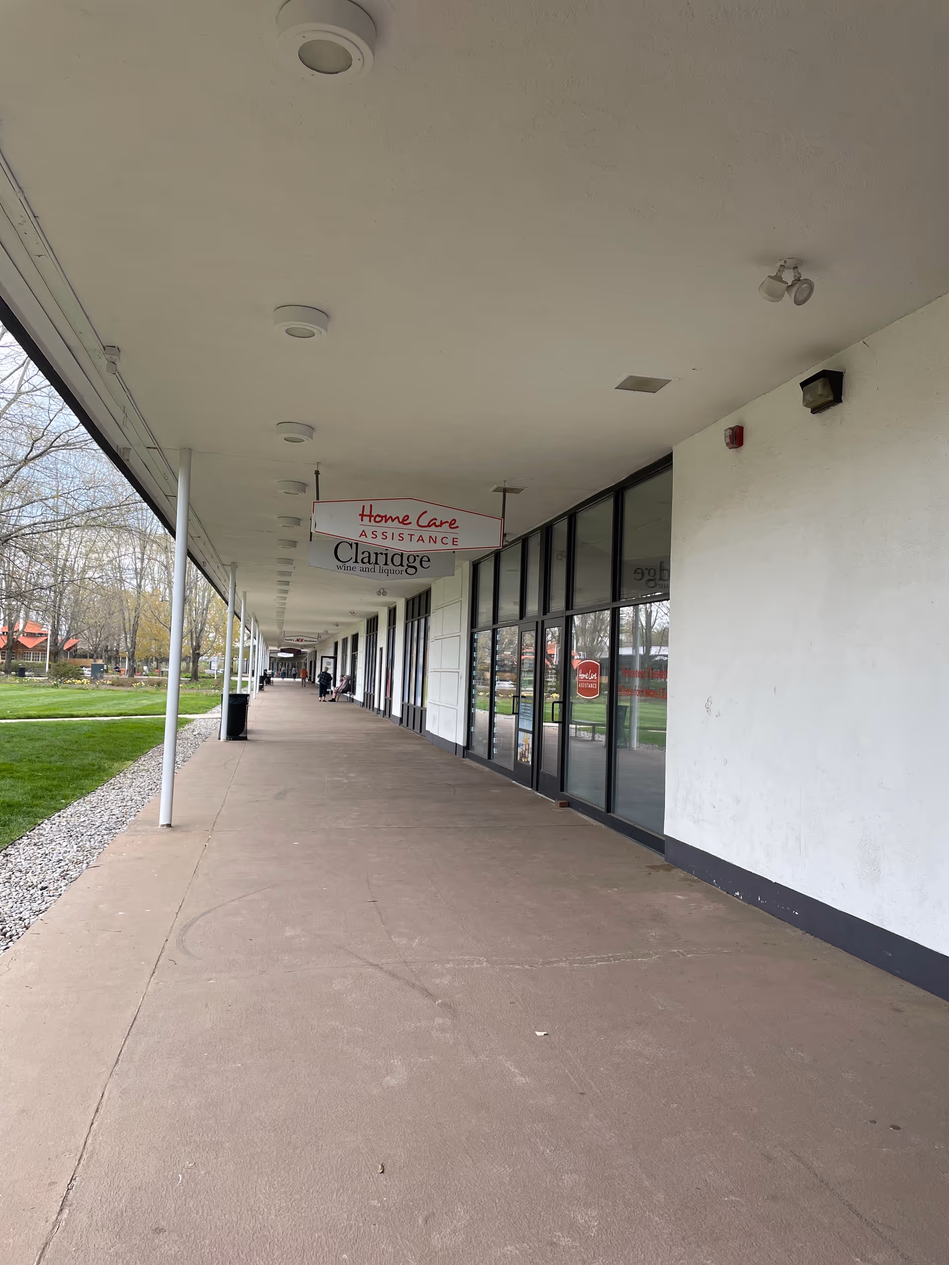 Long covered outdoor walkway with glass storefronts and a Home Care Assistance sign.