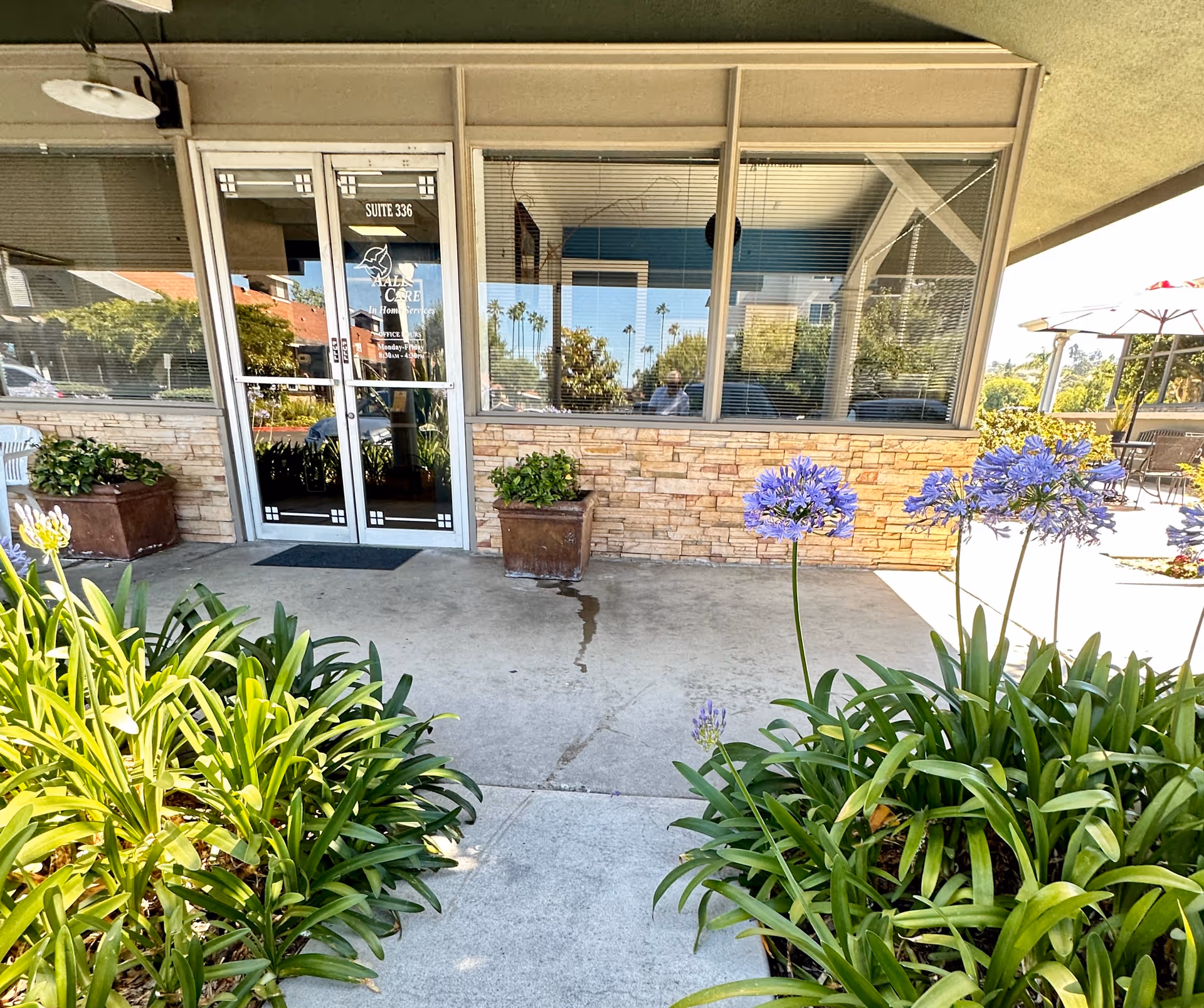 Front entrance of a senior care facility with glass doors, stone wall, and potted plants.
