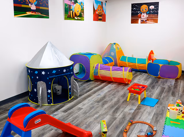 Colorful children's playroom with tents, tunnels, and toy furniture on a wood-like floor.