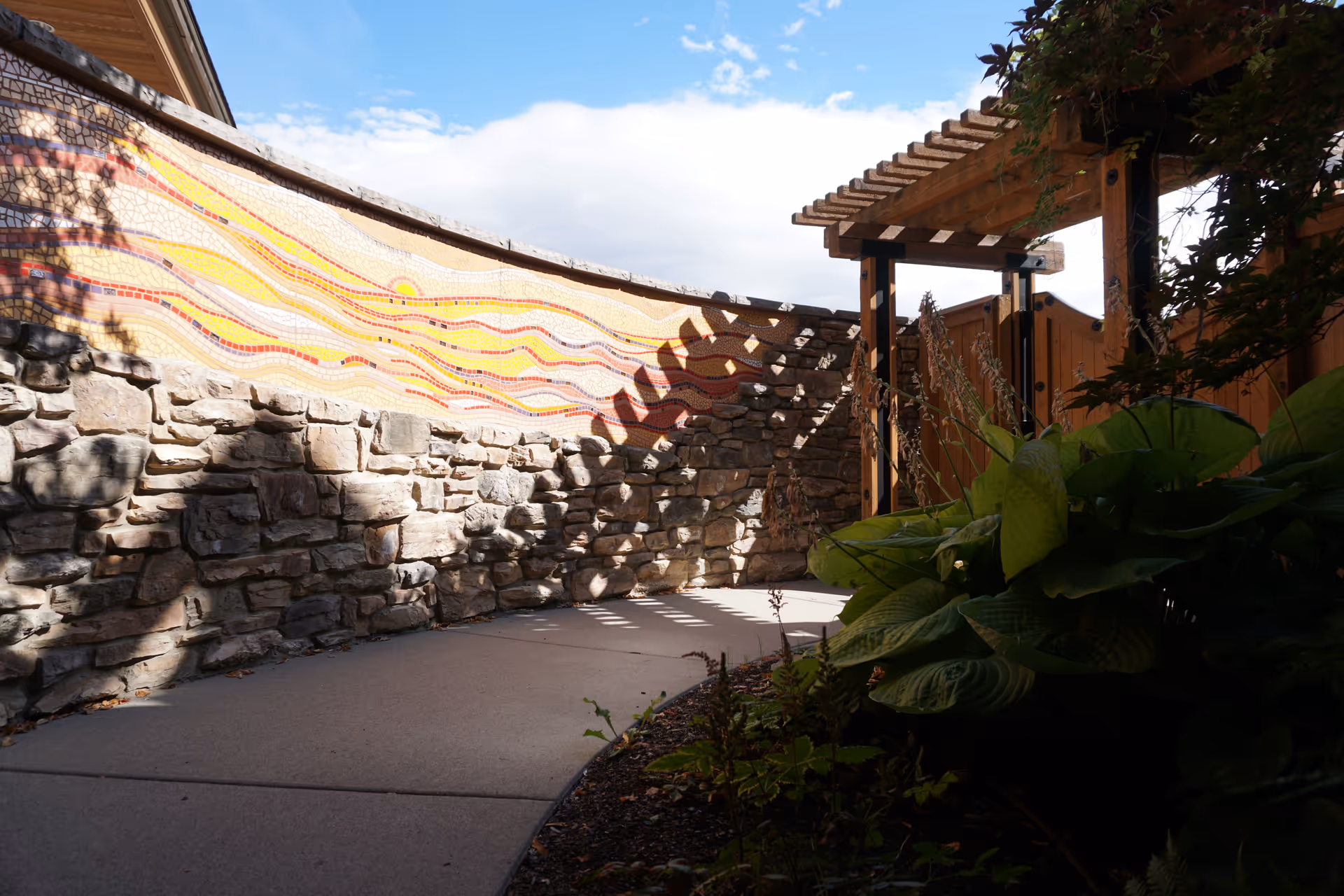 Outdoor walkway at Hospice of North Idaho featuring a mosaic wall and wooden pergola.