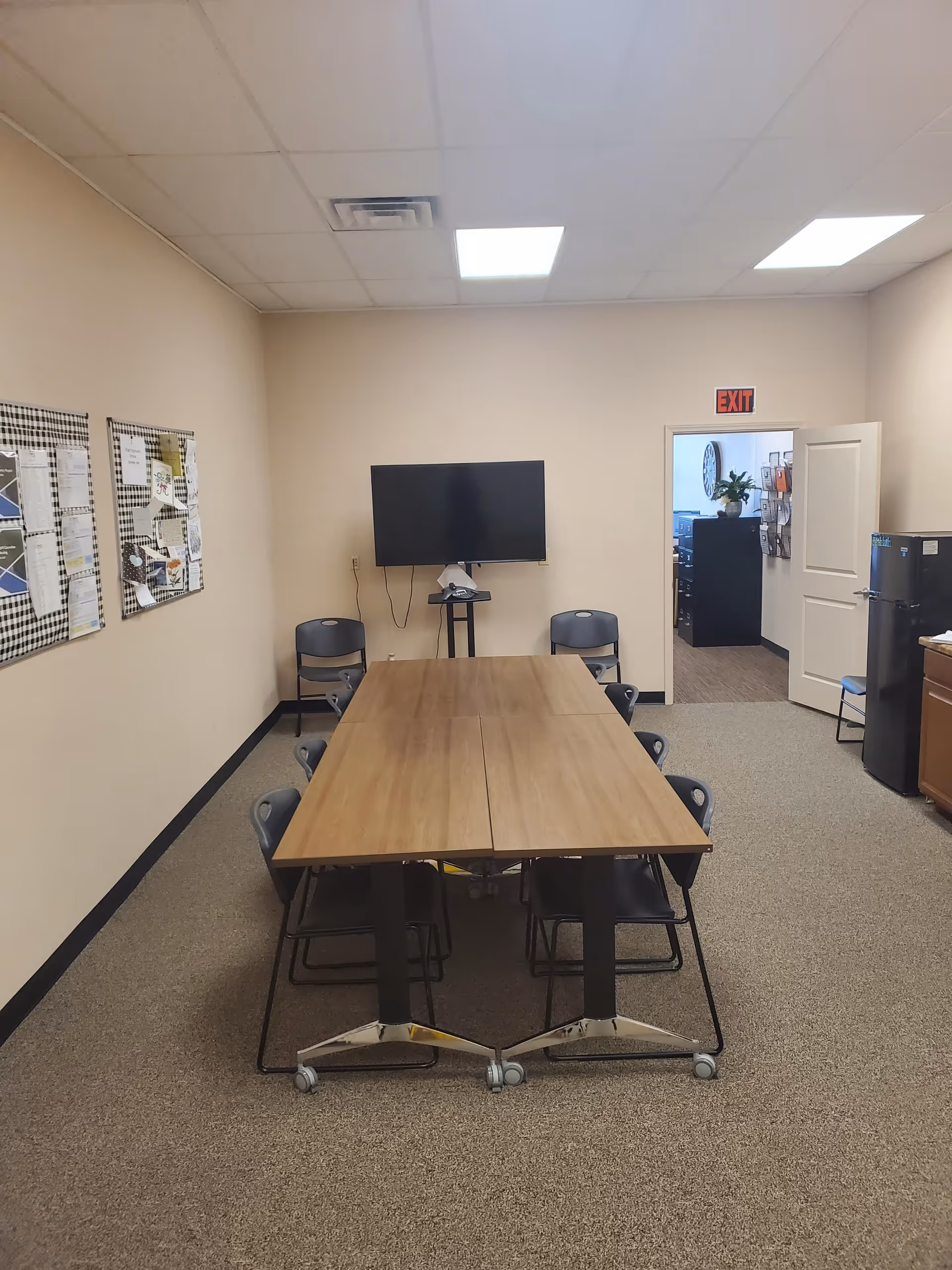 A long wooden table with chairs and a wall-mounted TV in a beige interior room.