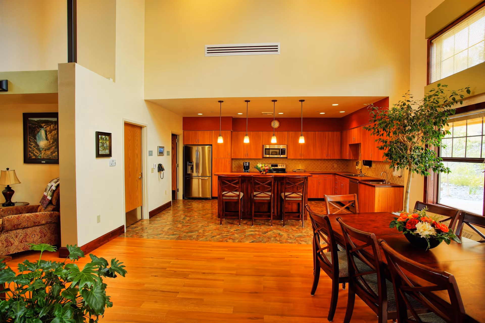 Open-concept common area with kitchen island, dining table, bar stools, and large windows.