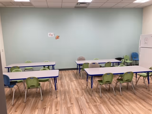Bright, empty dining area with blue tables and green chairs arranged in rows.