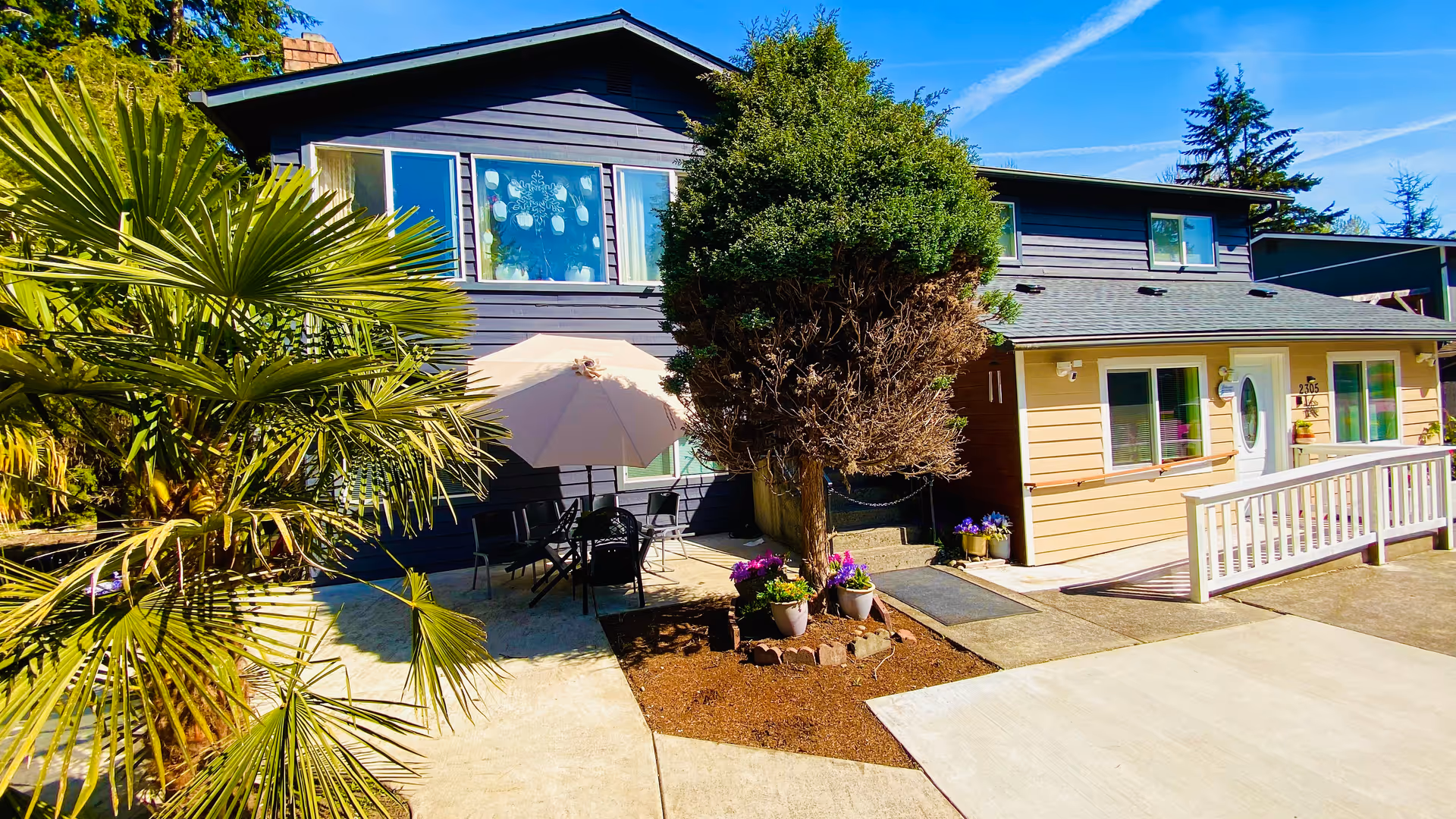 Exterior view of Blissful Living AFH with outdoor seating, umbrella, and potted plants.