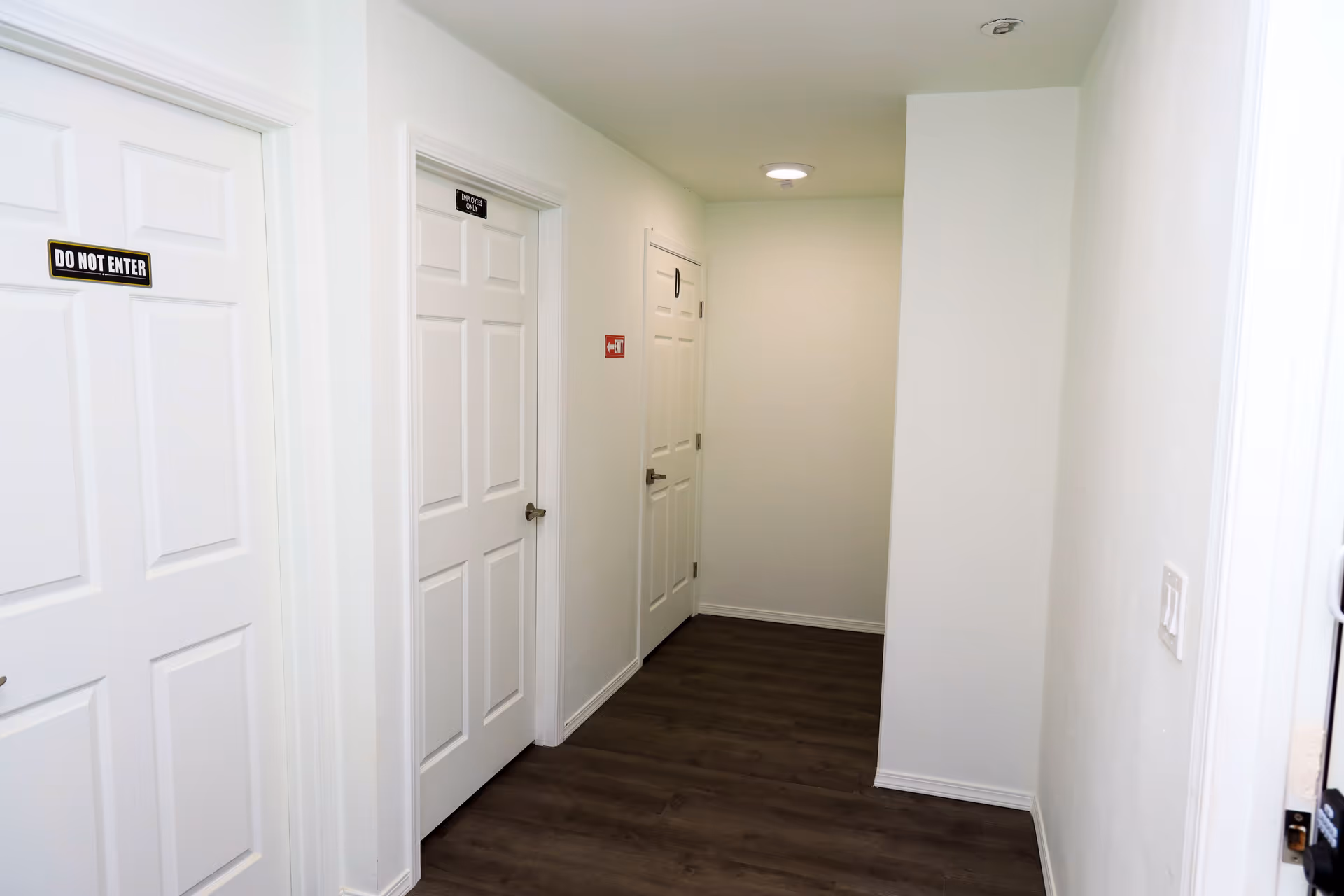 White hallway with multiple doors, dark wood flooring, and a Do Not Enter sign.