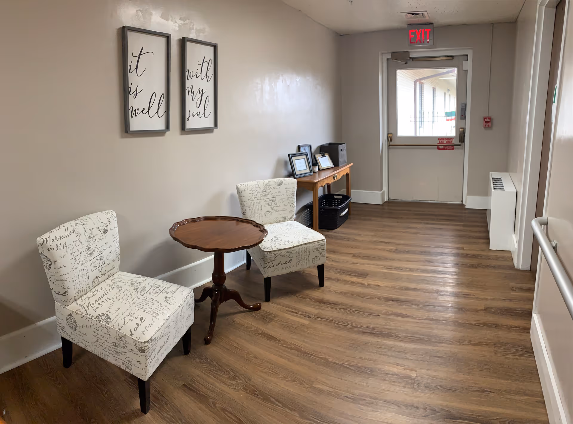 Two patterned chairs and a small table sit in a hallway seating area near the exit.