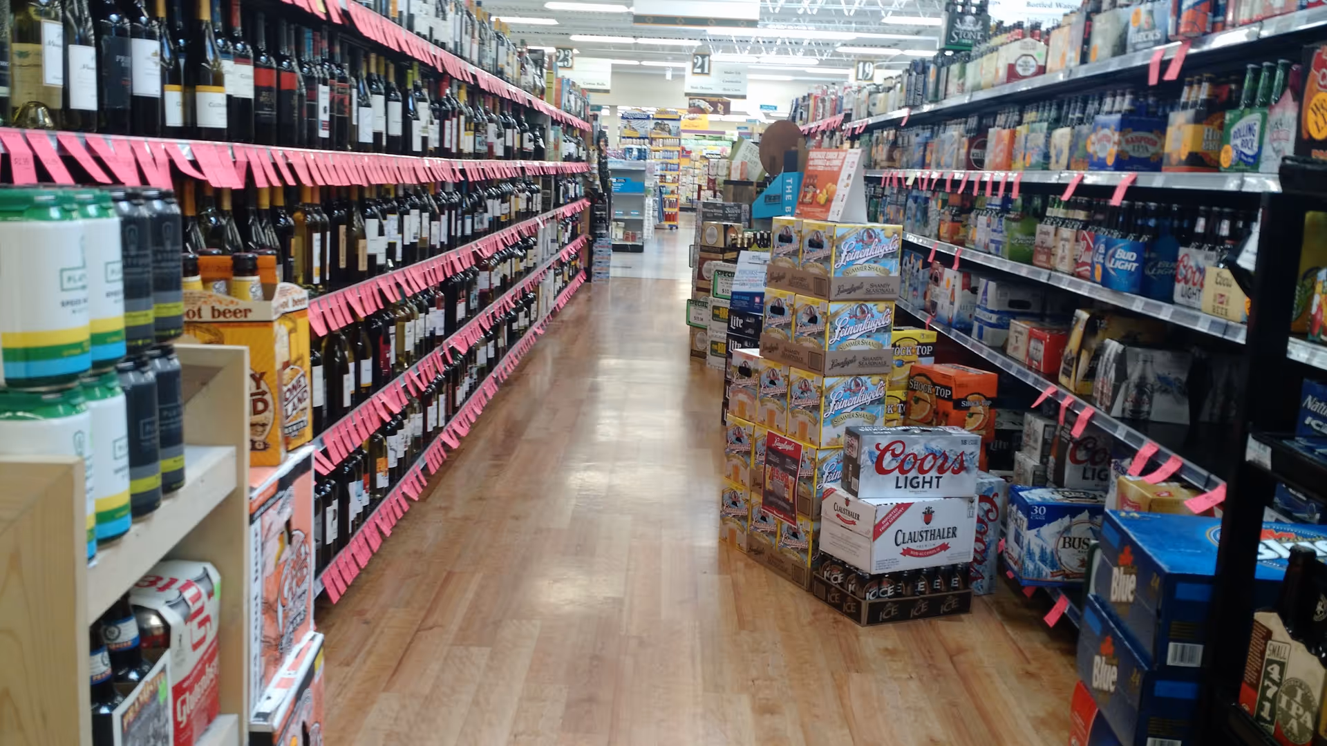 Narrow store aisle lined with shelves of bottles and pink price tags.