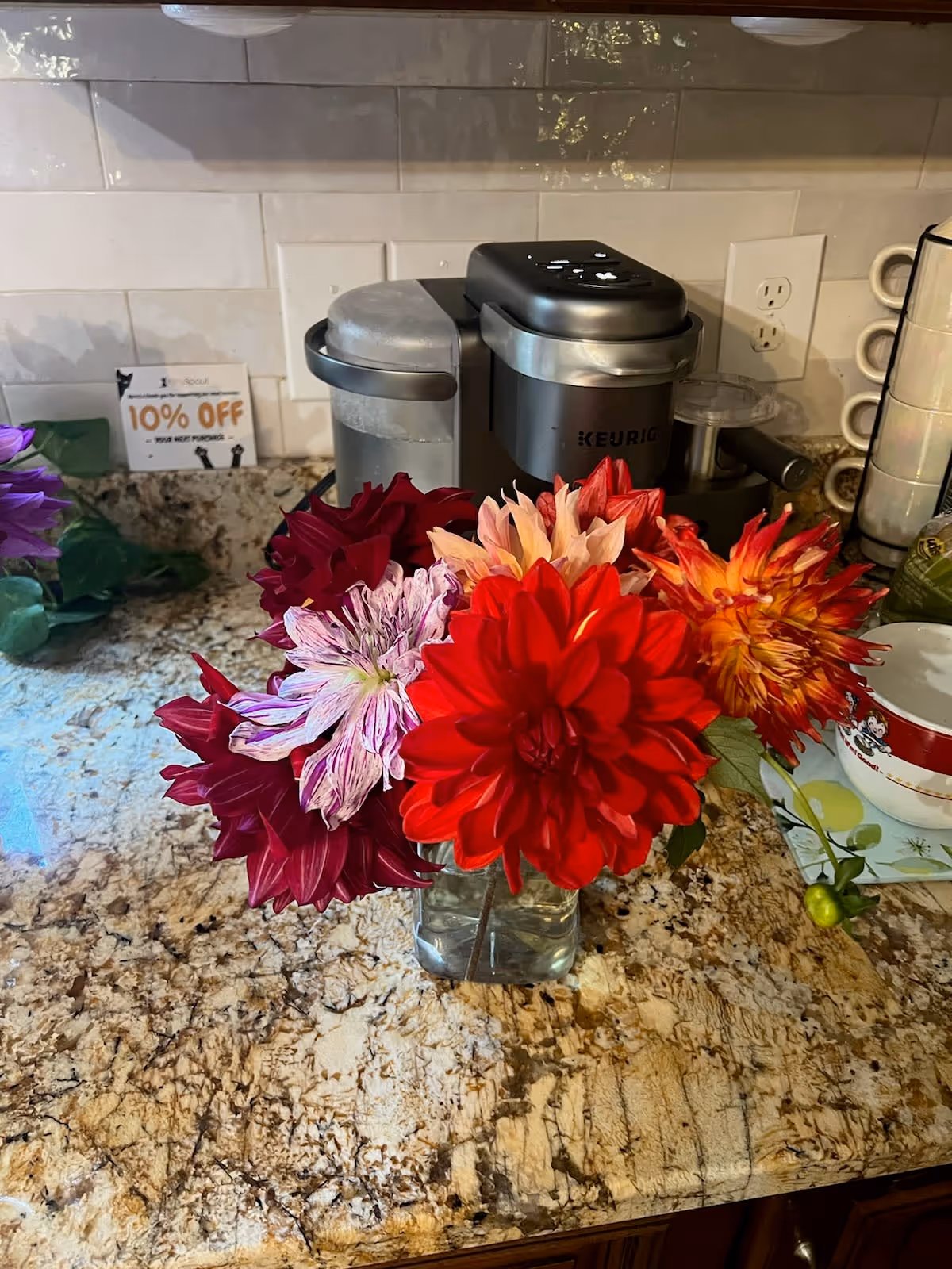 Flower bouquet in a glass vase sits on a granite kitchen countertop with a coffee maker.